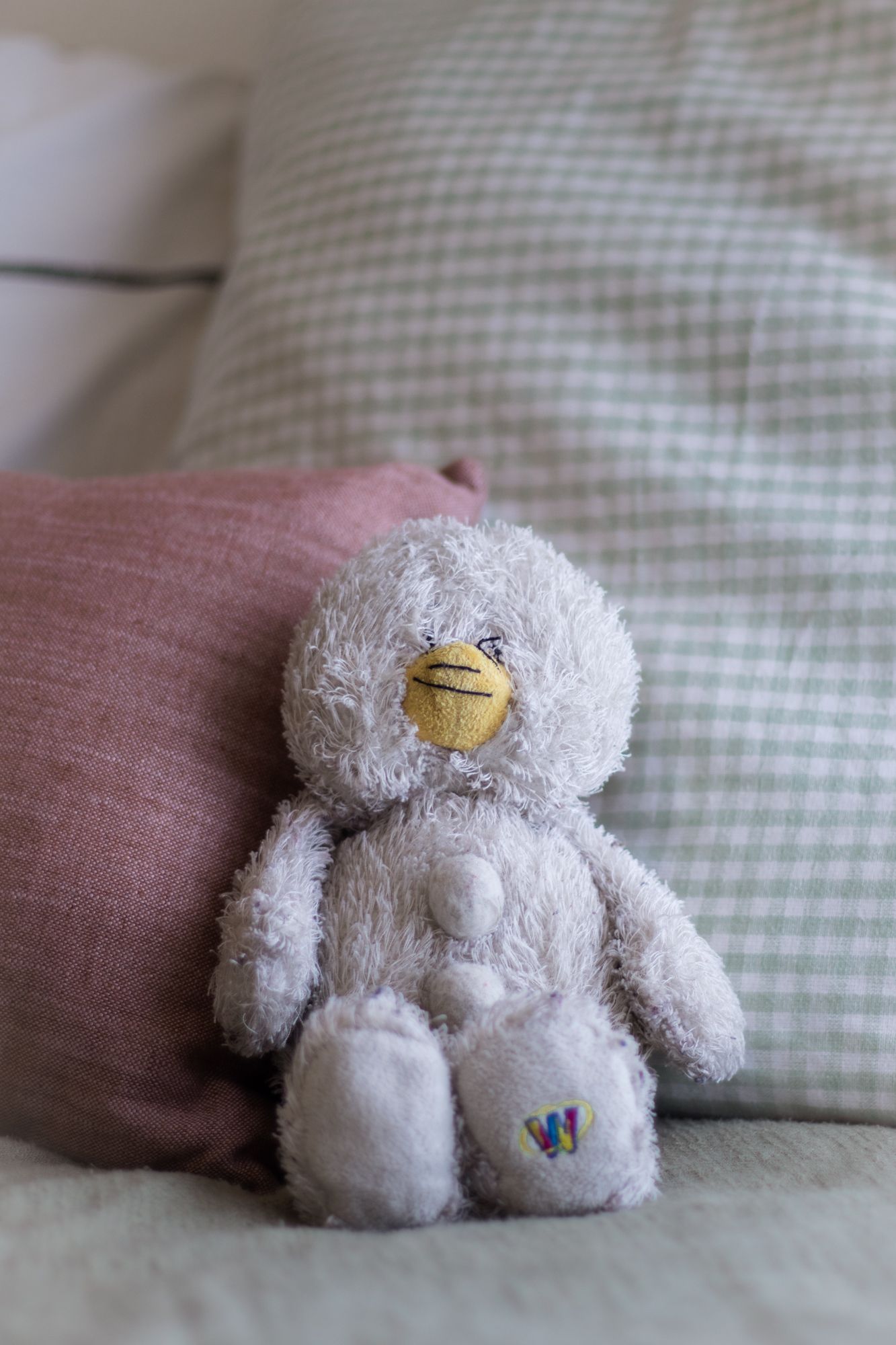 Charming lifestyle photography of a plush toy among textured pillows, featuring soft natural light and a cozy, nostalgic home aesthetic.