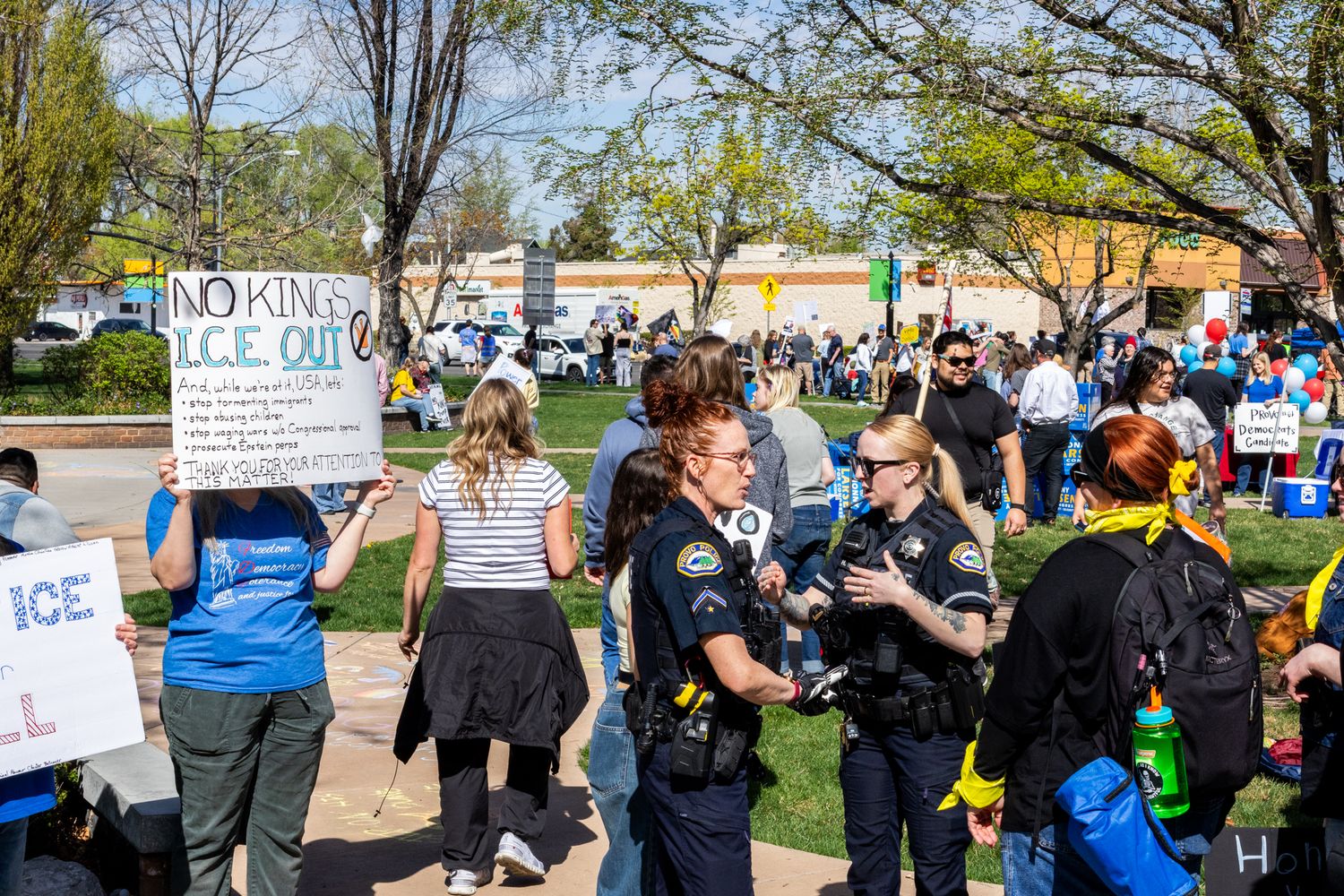 A candid documentary photograph of local law enforcement interacting with community members at a public demonstration in a city park.