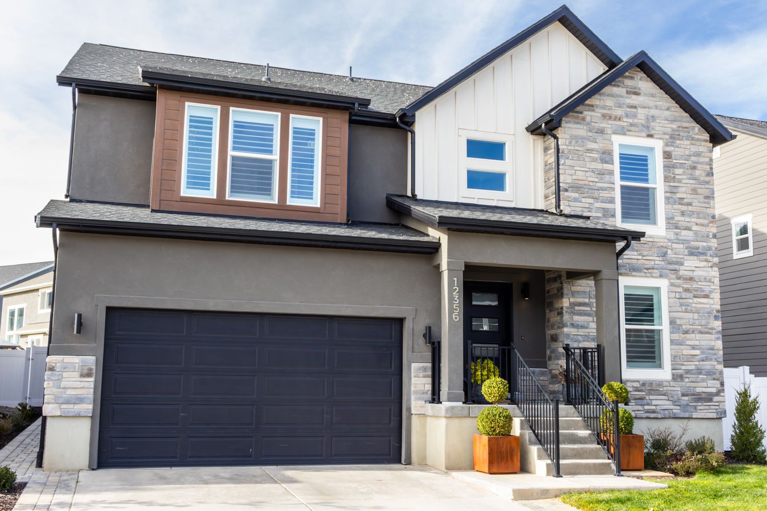 High-end real estate photography of a modern two-story home, showcasing mixed-material siding, stone accents, and professional landscaping.