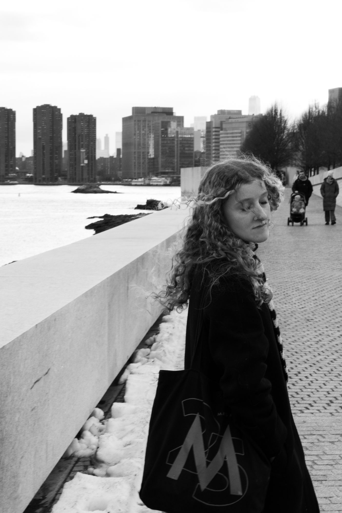 Moody B&W portrait of a woman on a city waterfront. High-contrast urban aesthetic. Professional photography for artists and creative bios.