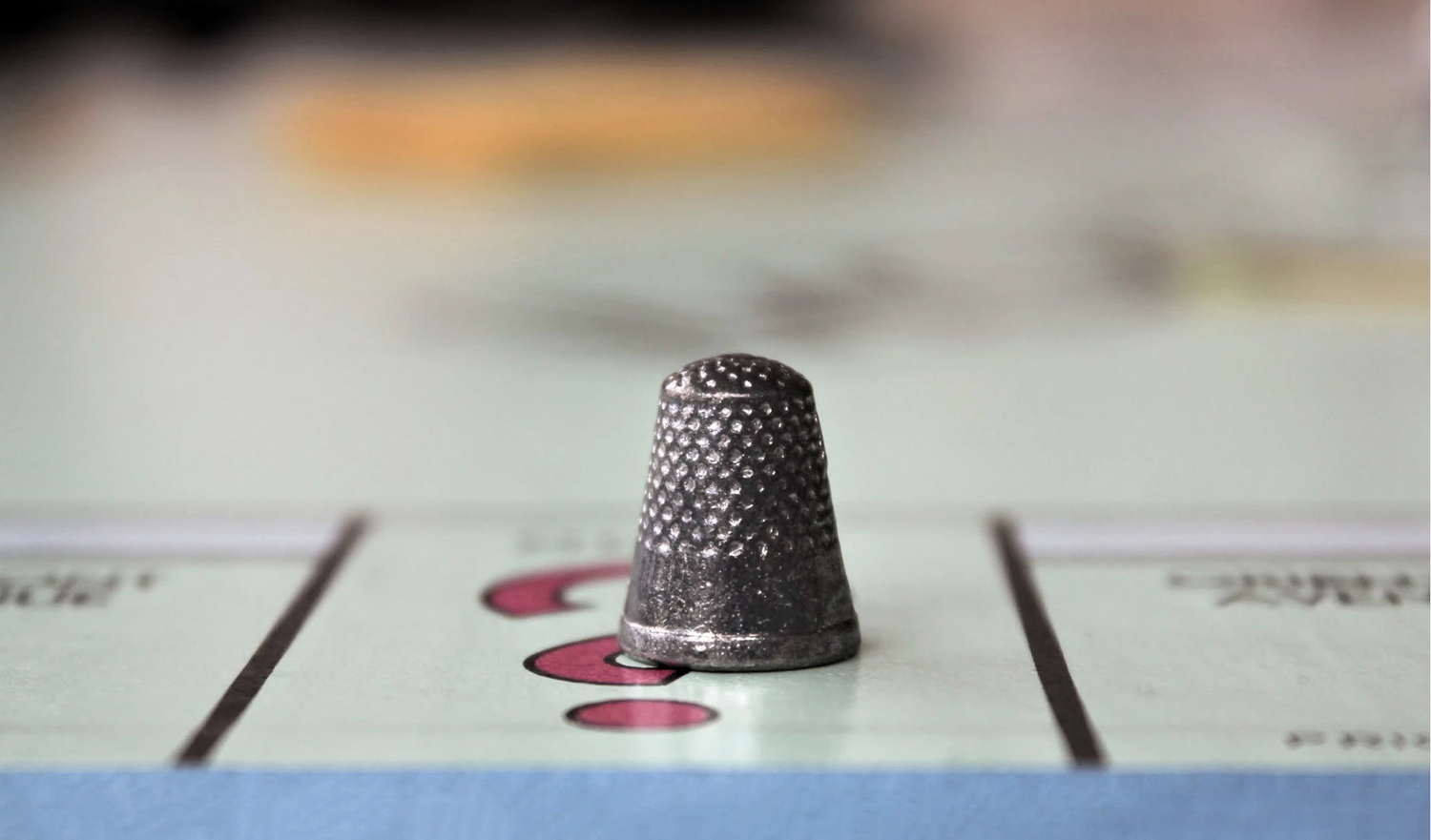 Macro photography of a vintage Monopoly thimble on a game board, featuring a shallow depth of field to highlight intricate metallic texture.