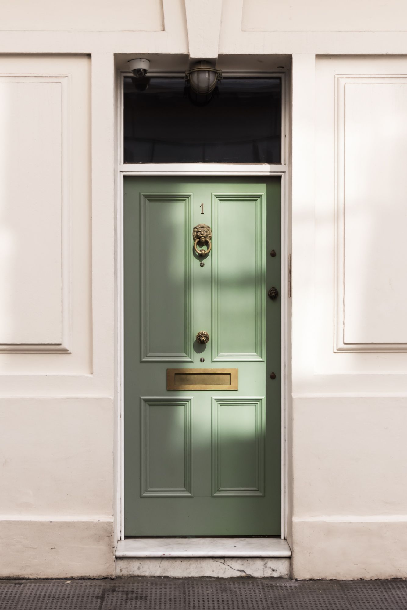 A study of a sage green Georgian door. Focus on the symmetrical paneling and the brass lion-head knocker. Architectural imagery.
