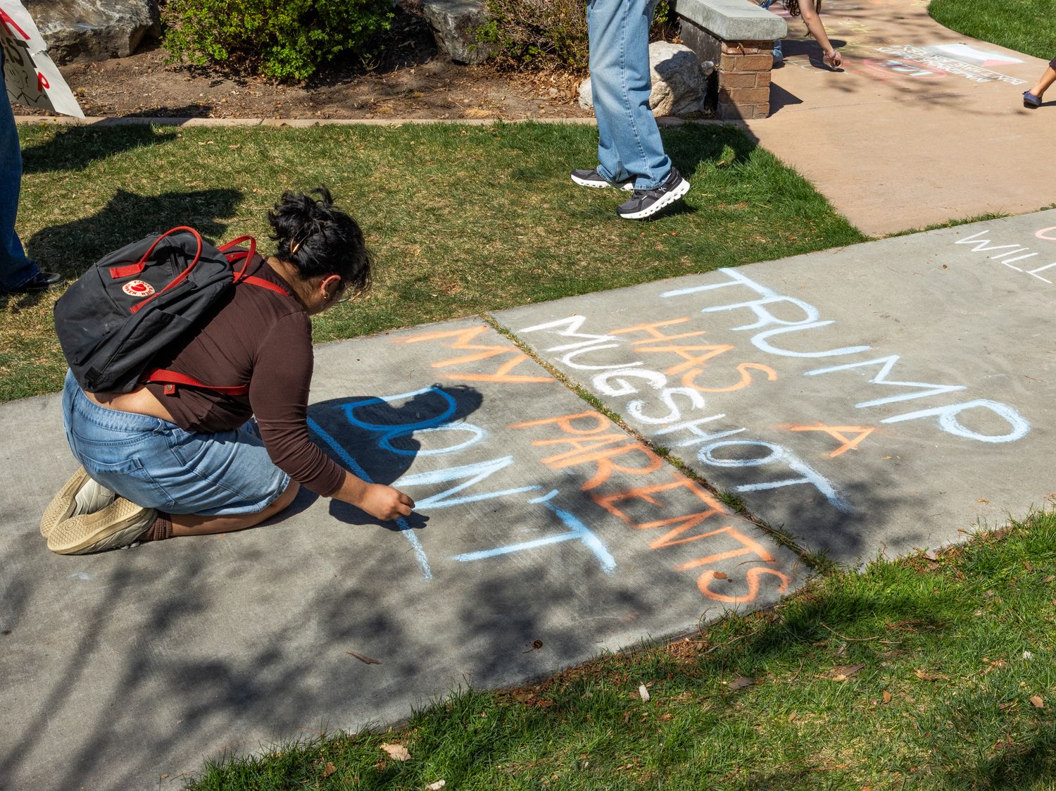 A high-angle documentary shot of an individual creating chalk art on a sidewalk, using colors to share a personal and political message.