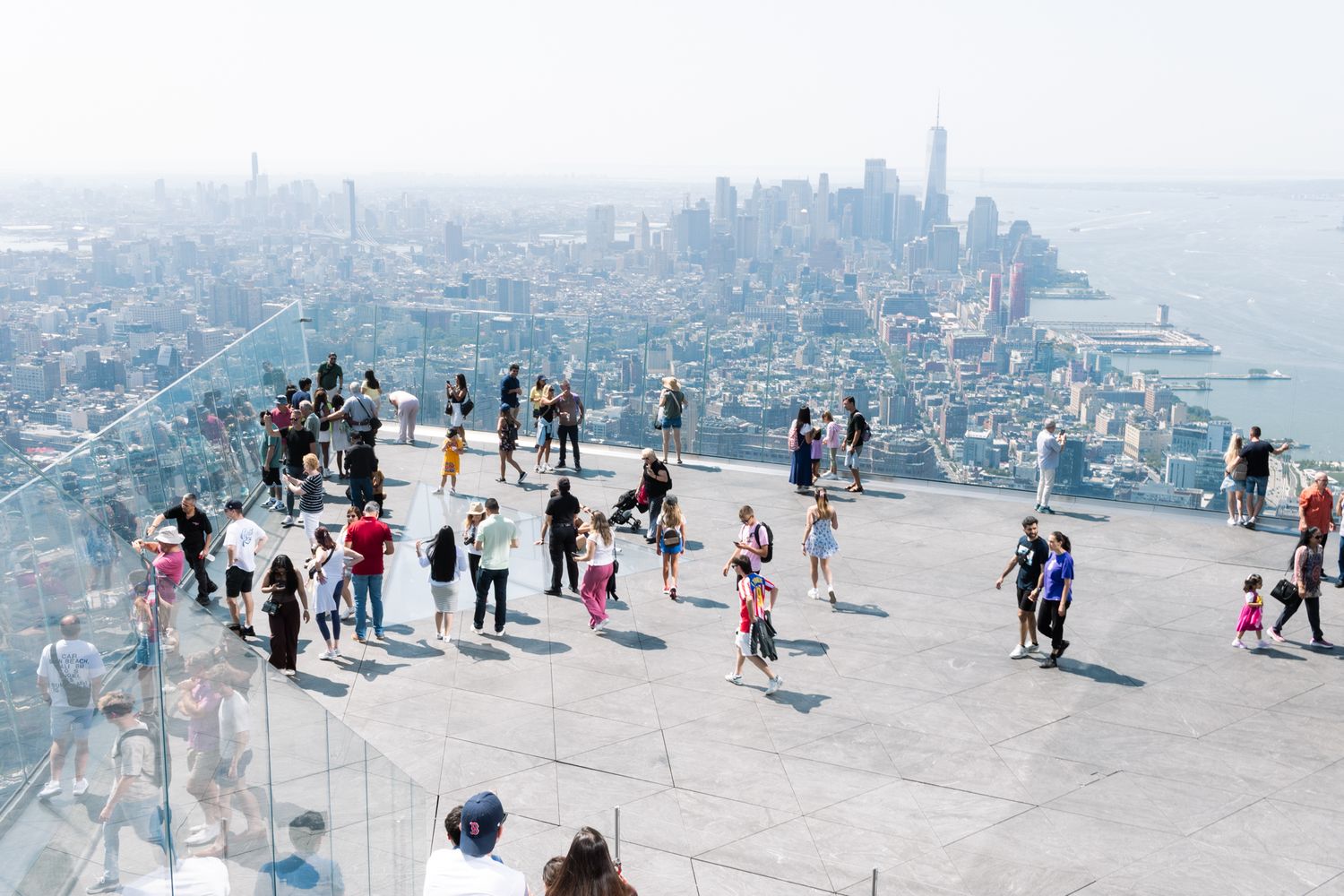 Tourists take in breathtaking 360-degree views of the Manhattan skyline and One World Trade Center from a glass-walled observation deck.