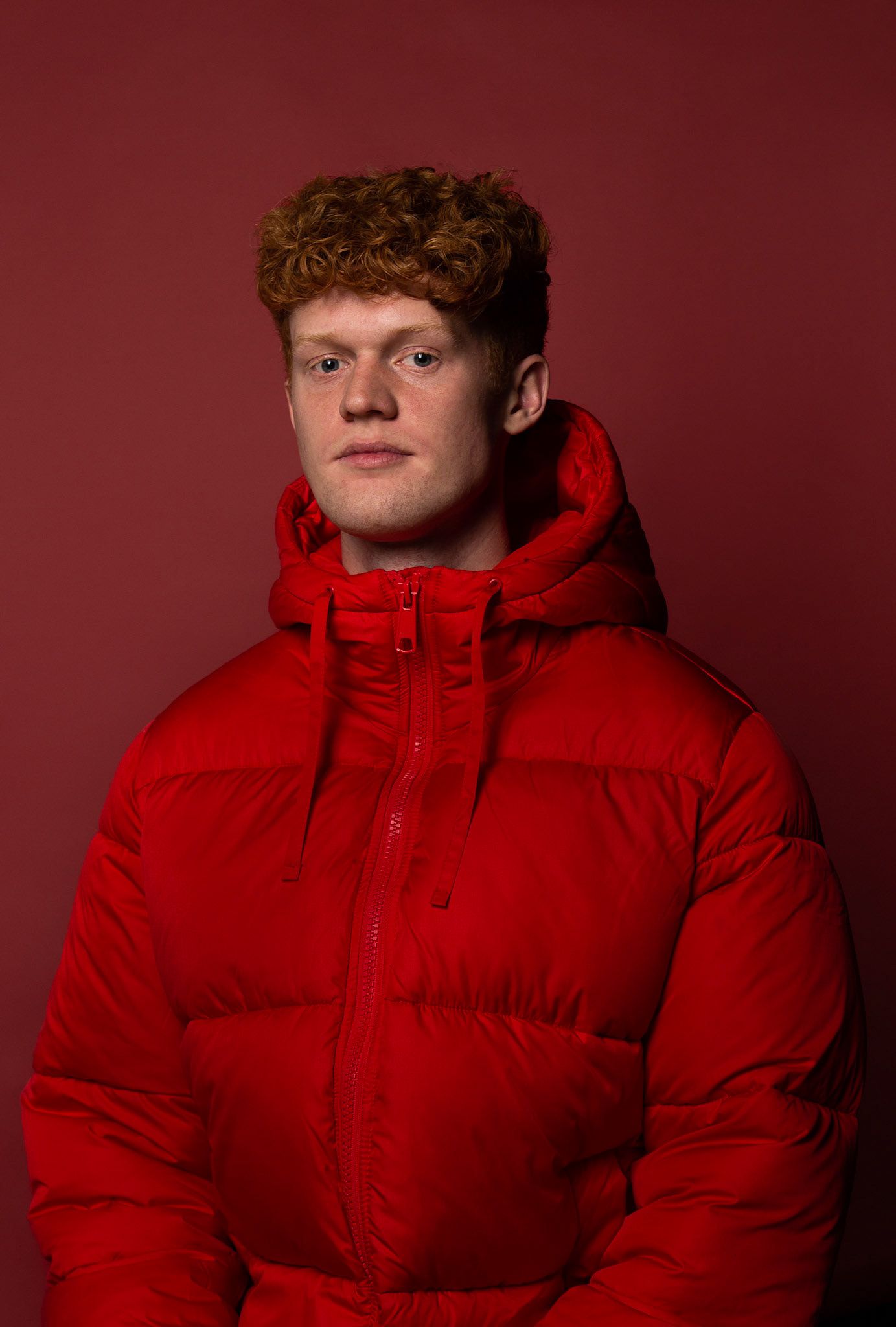 Bold red-on-red fashion portrait featuring a puffer jacket and studio lighting, showcasing expertise in color theory and commercial apparel.
