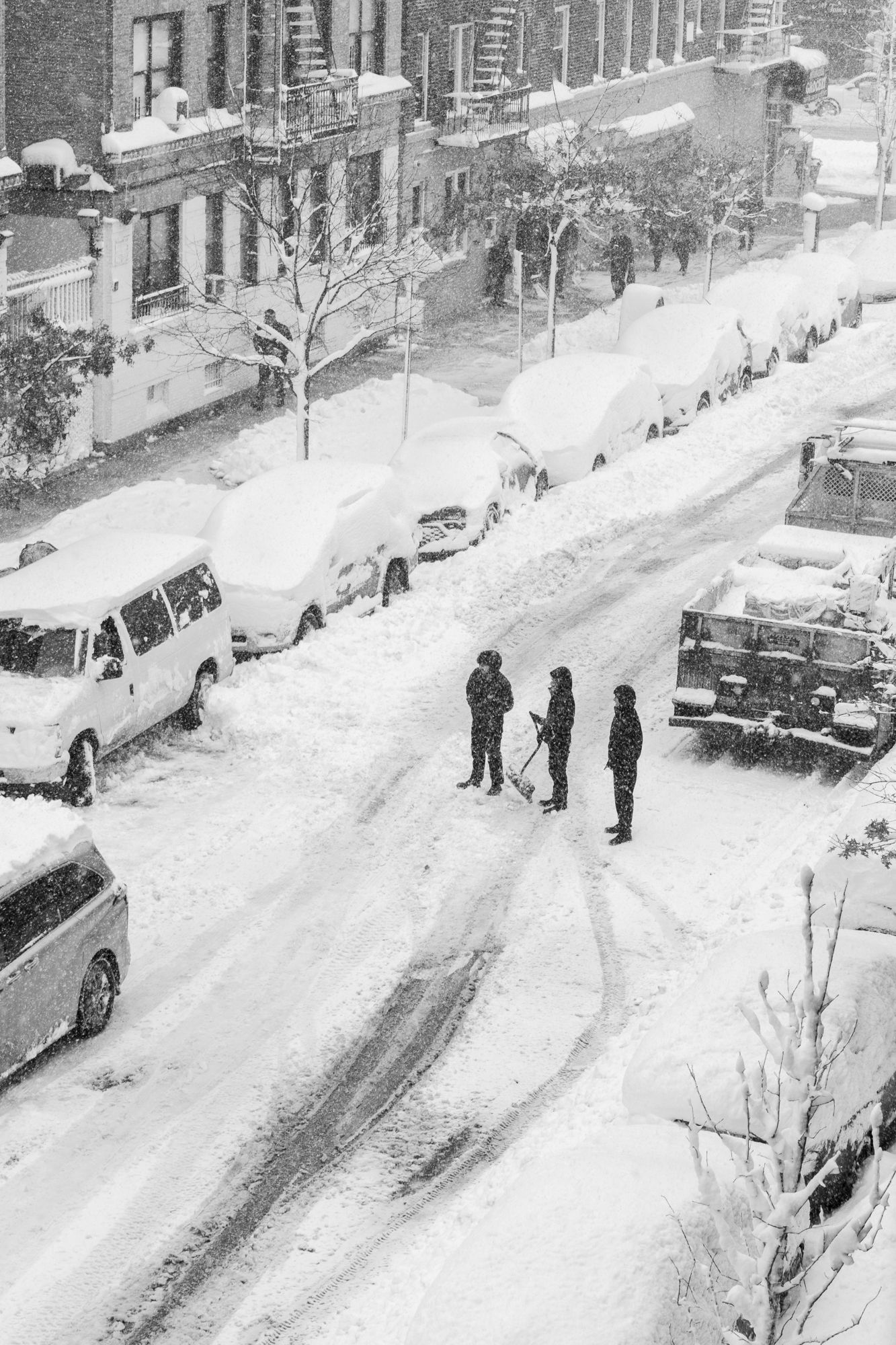 Candid B&W urban winter scene. Neighbors shoveling a snowed-in city street. Authentic documentary photography for news and editorial use.