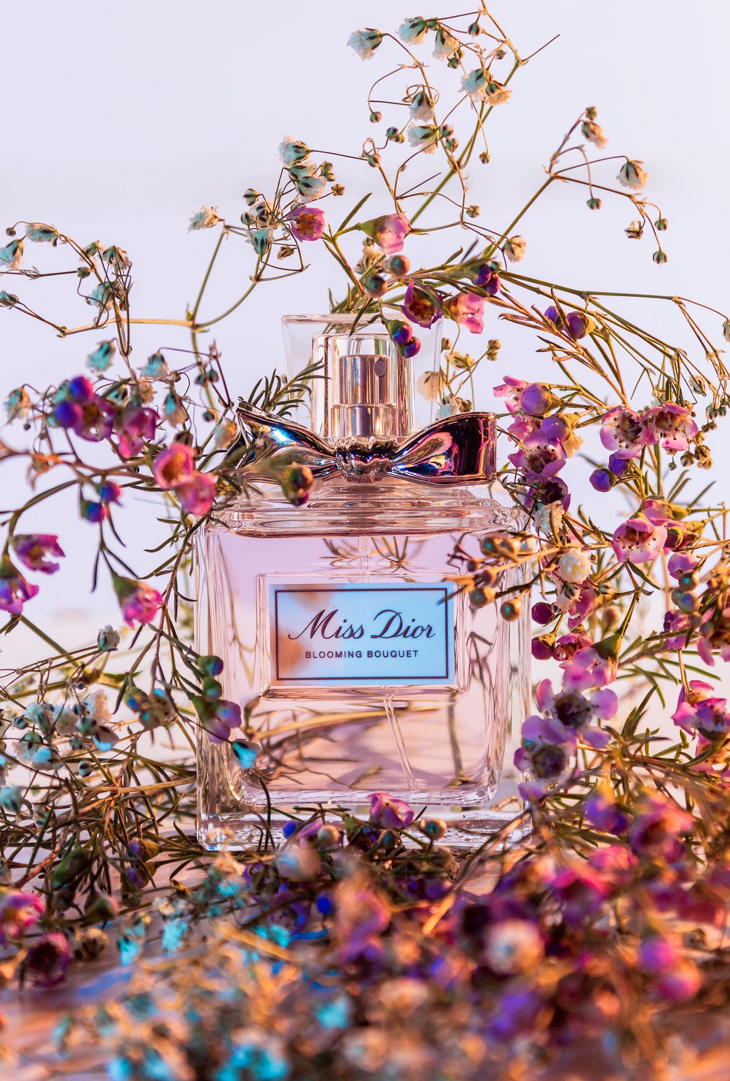 Dreamy perfume product photography featuring Miss Dior Blooming Bouquet surrounded by wildflowers, highlighting delicate floral notes