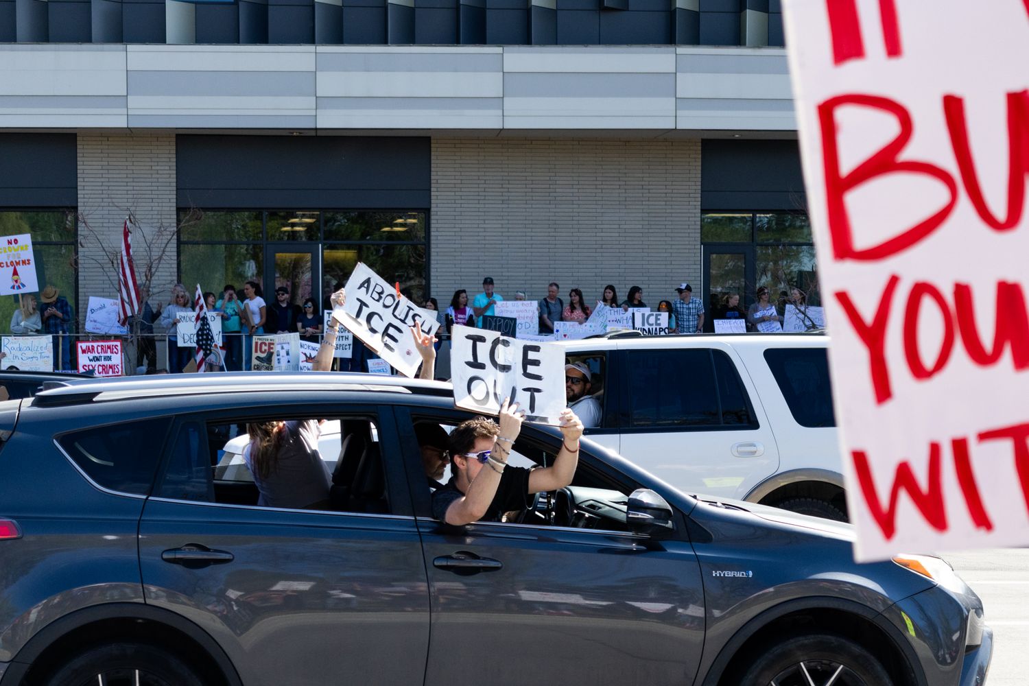 A dynamic documentary shot capturing demonstrators holding signs from car windows, showcasing a mobile protest and local civic engagement.