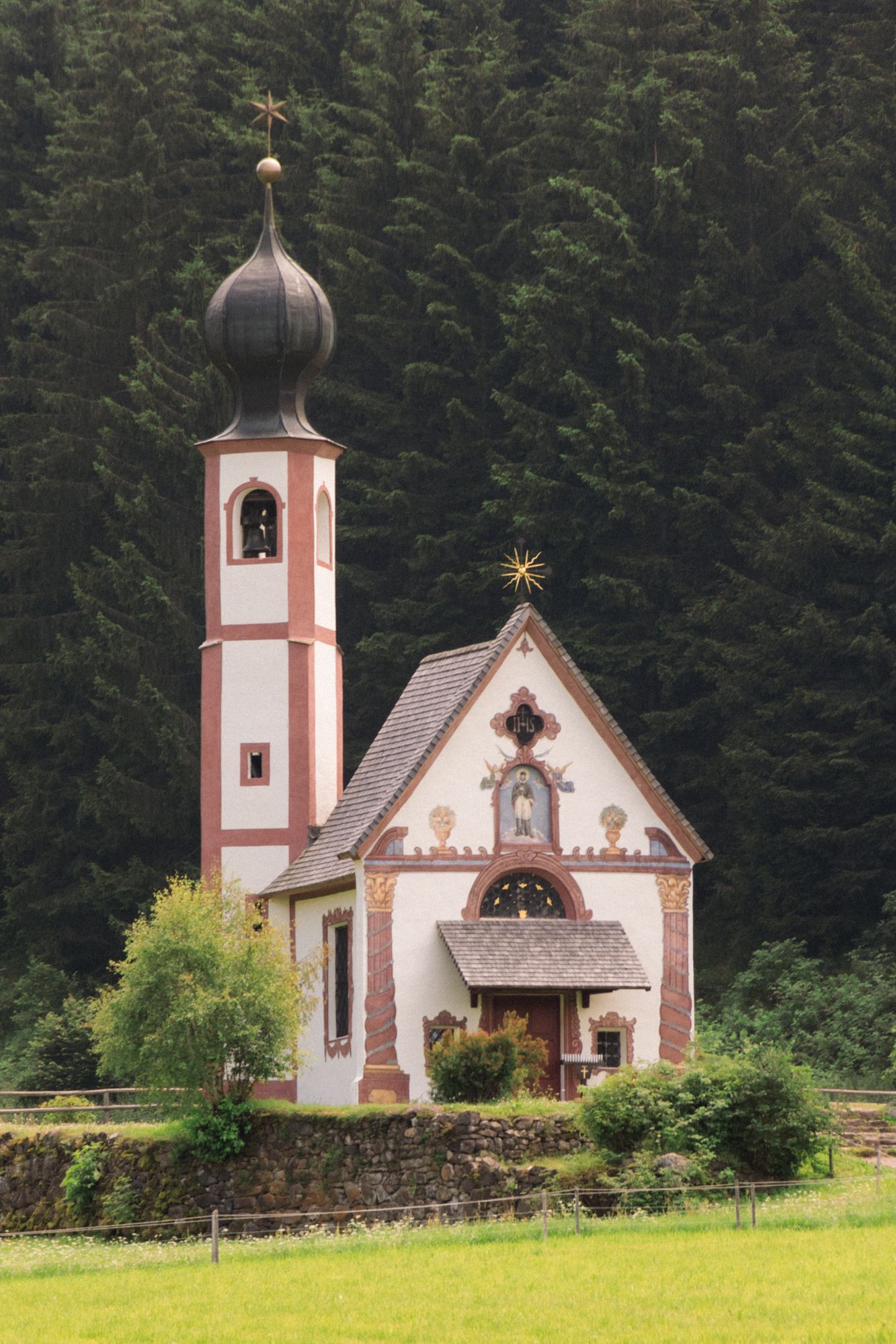 Discover the serene beauty of St. Johann in Ranui, a landmark Baroque chapel nestled against the dark evergreen forests of Val di Funes.