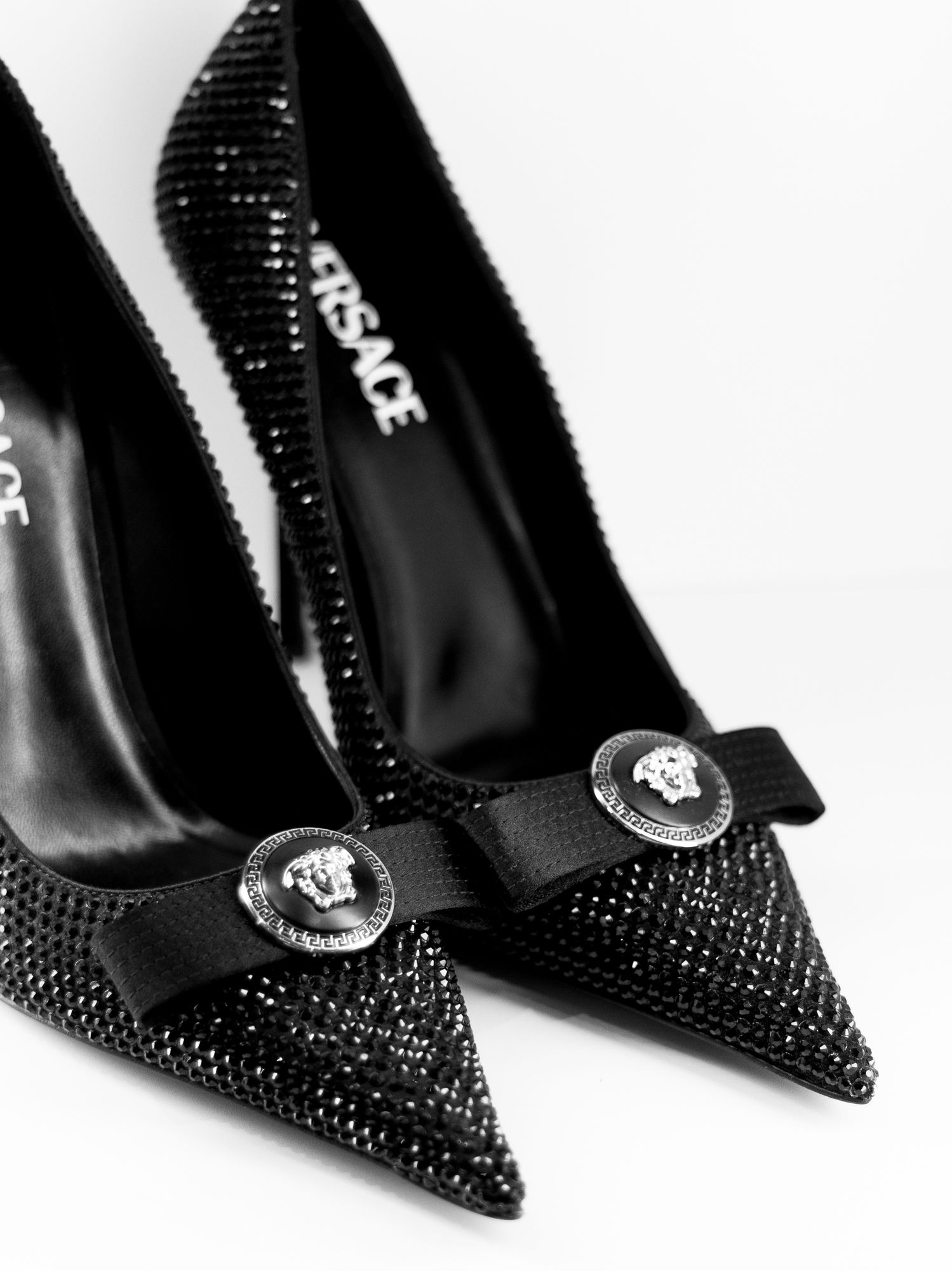 Elegant B&W luxury fashion photography of crystal-embellished Versace heels, highlighting iconic Medusa hardware and intricate textures.