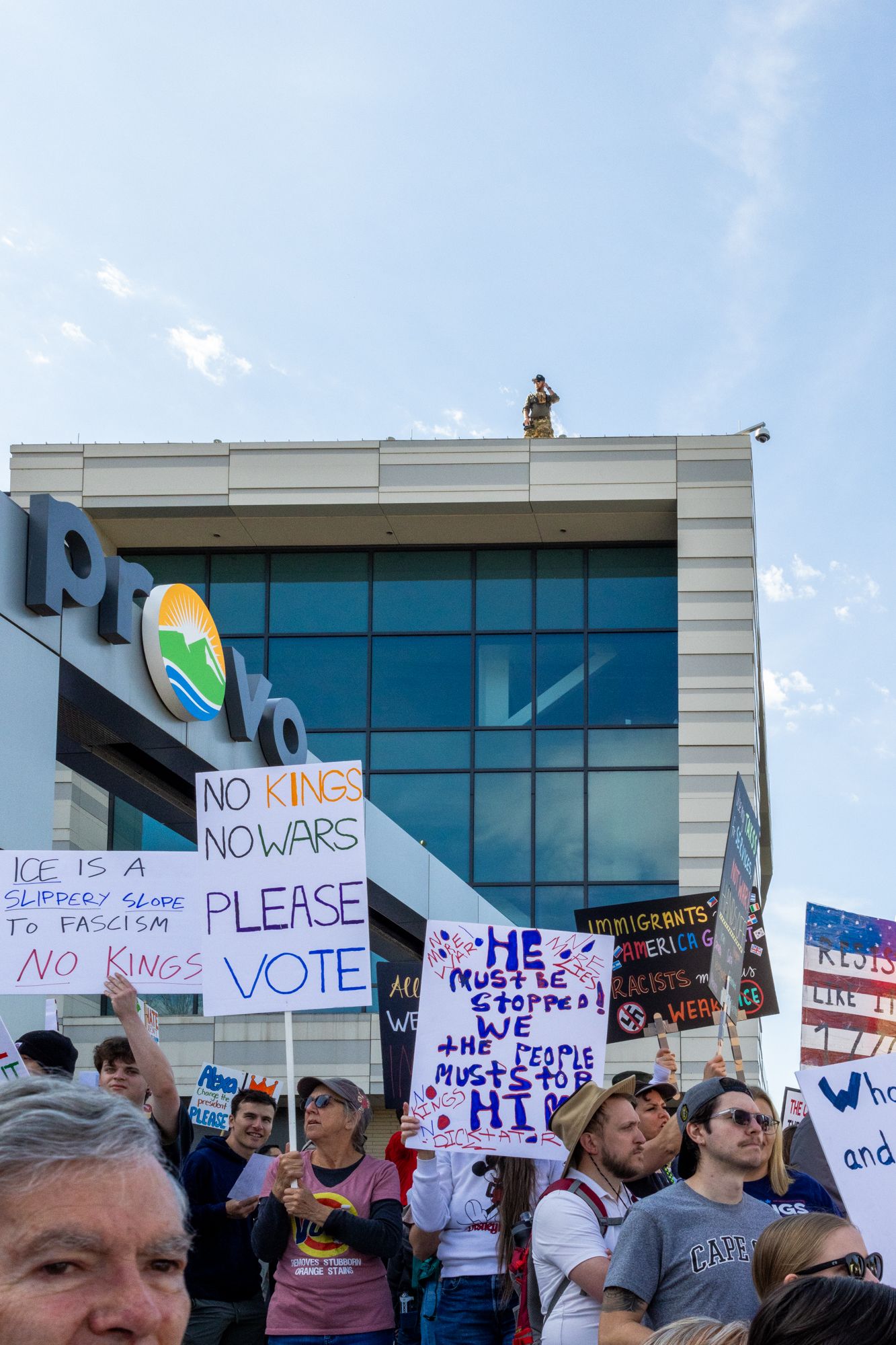 A low-angle documentary shot capturing a sea of hand-painted signs held by demonstrators in front of the Provo city emblem.