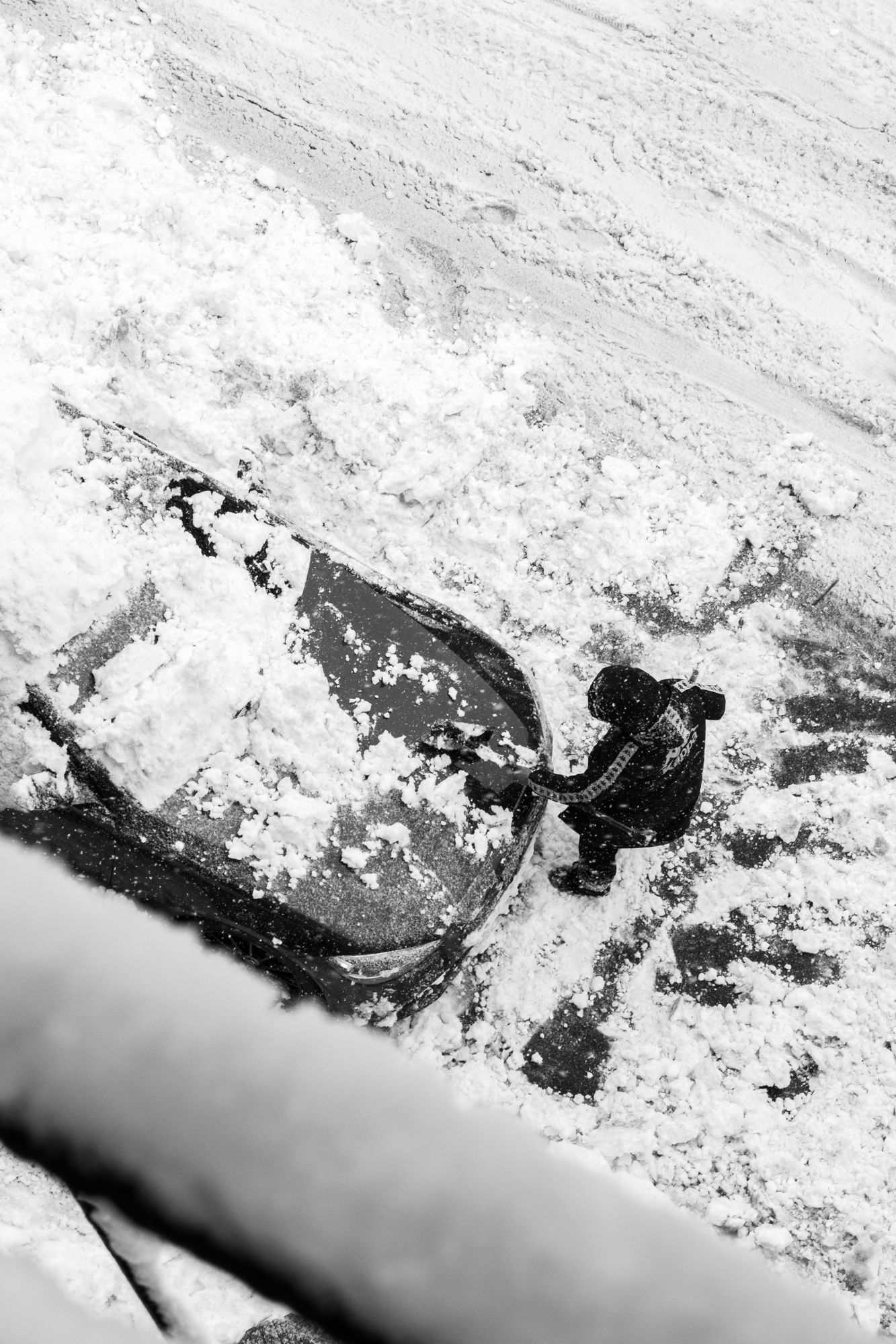 Gritty monochrome urban winter shot. Overhead view of the daily struggle in a snowstorm. Authentic stock imagery for blogs and media.