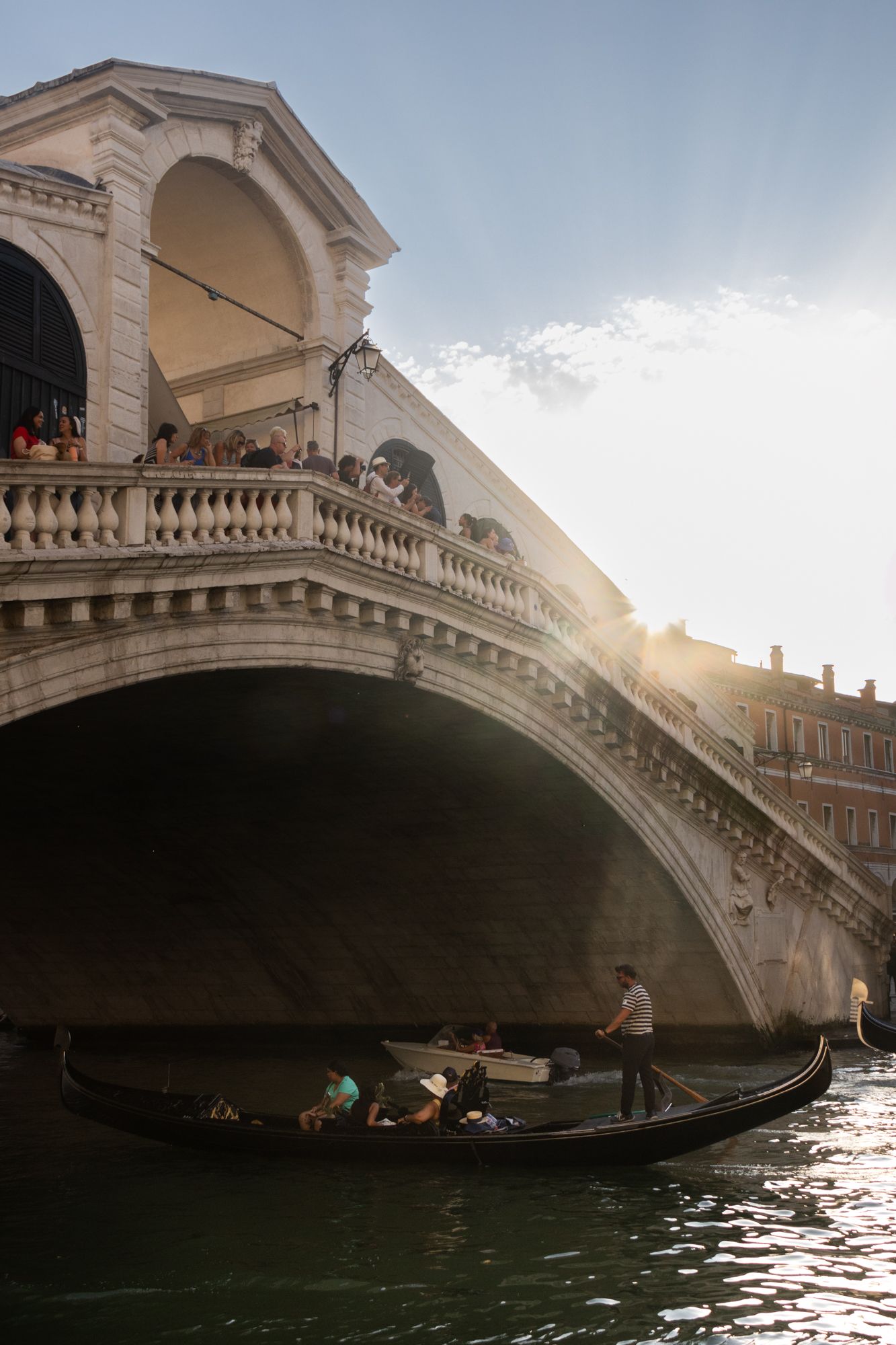 Golden hour light bathes the Rialto Bridge in Venice as gondolas pass beneath the stone arches of the Grand Canal during a warm sunset.