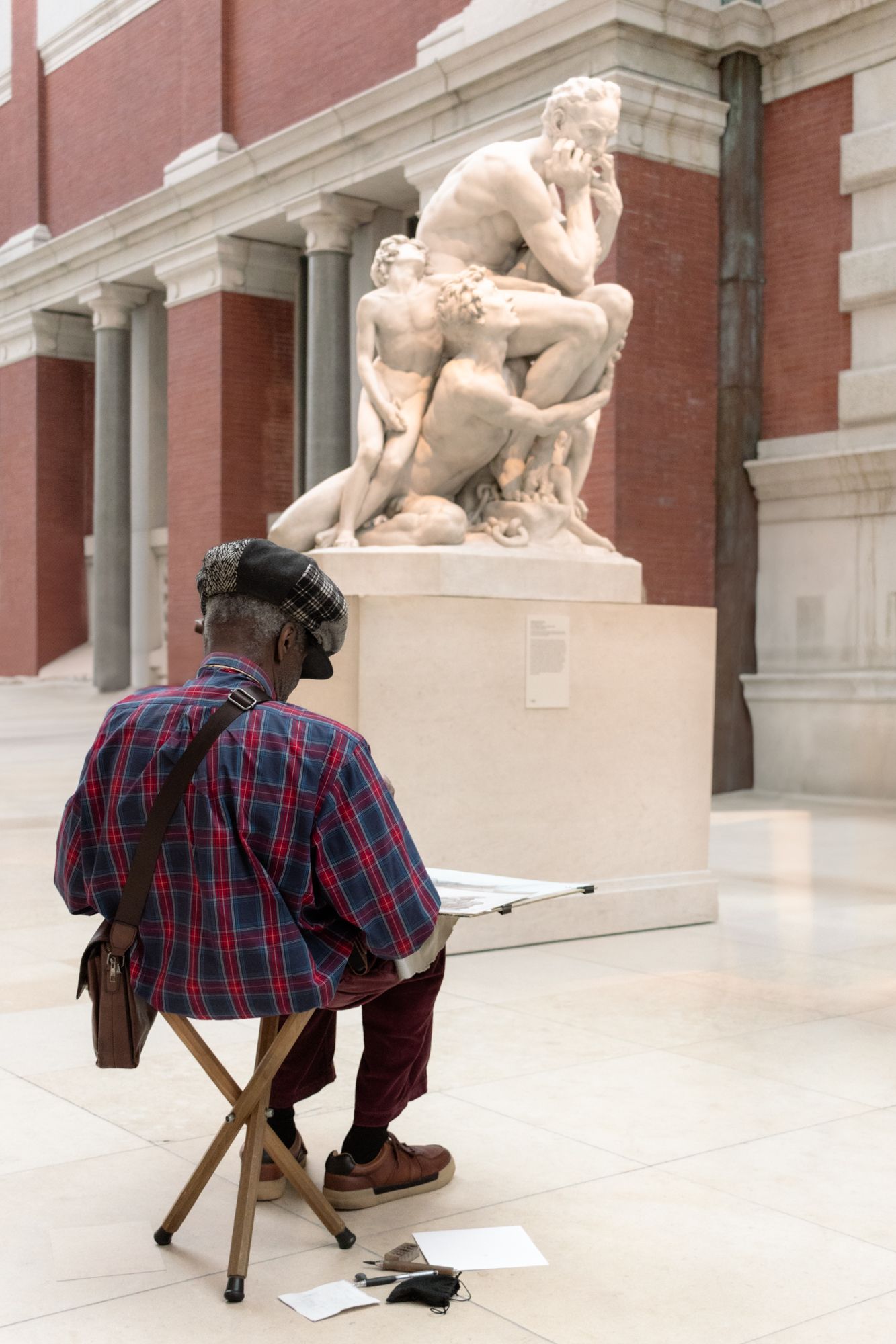 An artist sits on a bench in the sculpture gallery of The Met, sketching the powerful marble curves of Carpeaux’s Ugolino and His Sons.