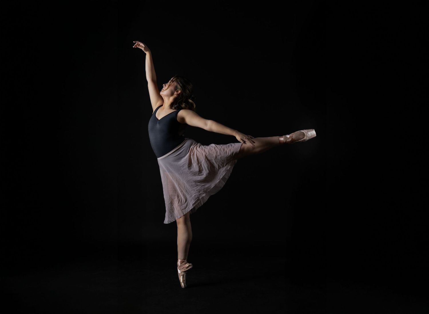Professional ballet studio photography. Elegant dancer in a leotard and skirt on black. High-quality imagery for dance resumes and schools.