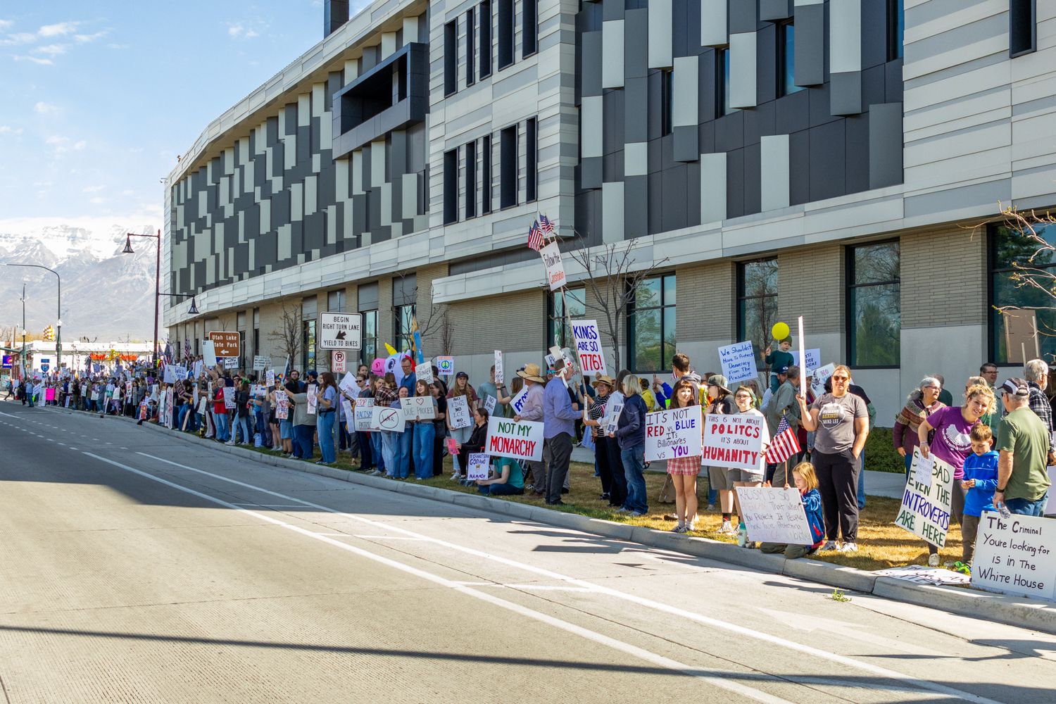 A wide-angle documentary shot capturing the scale of the demonstration as protestors line the sidewalk of a modern city block.