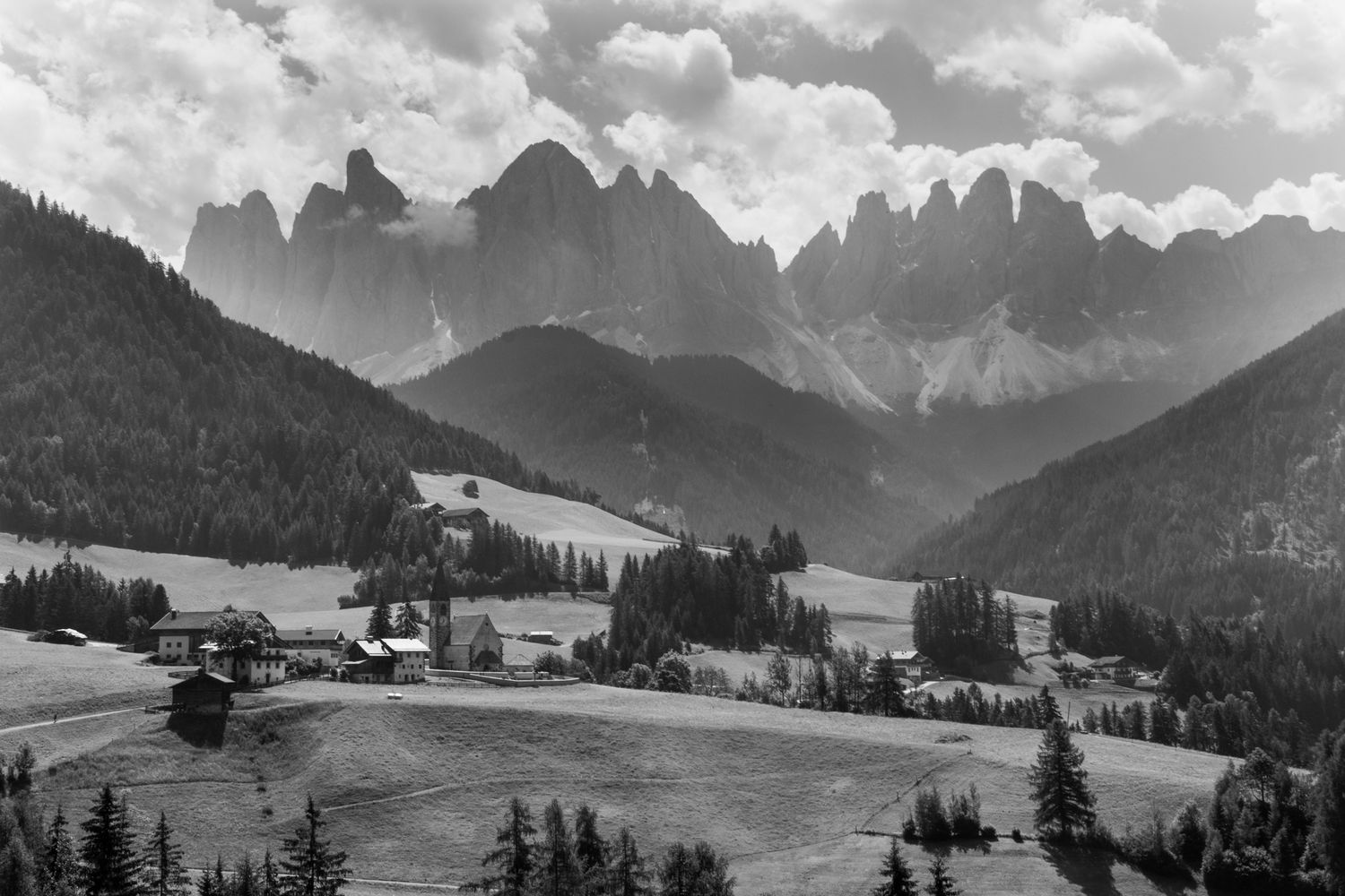 Dramatic black-and-white landscape of the Odle Mountains towering over a serene Val di Funes valley. Timeless Alpine photography at its best