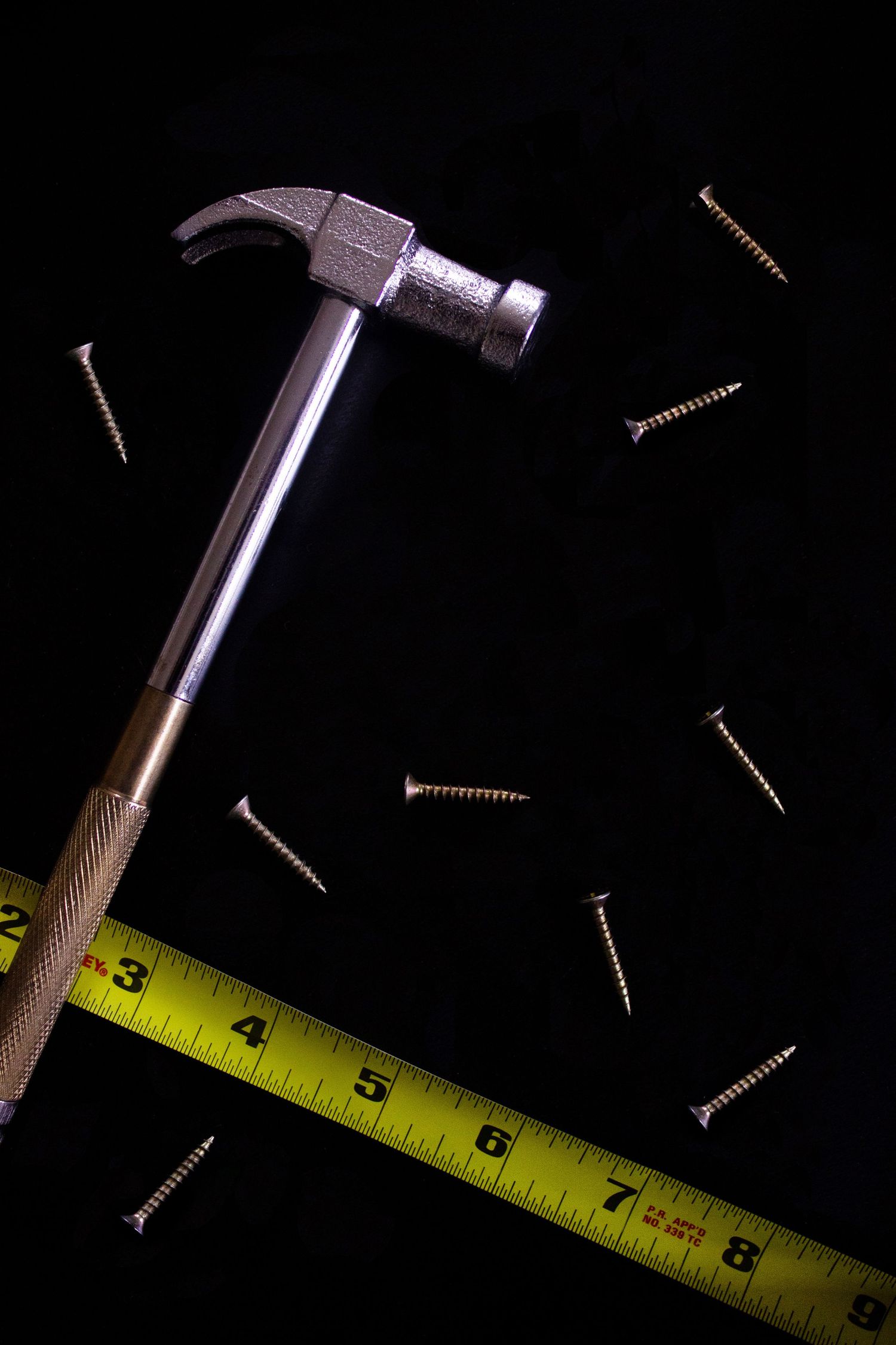 Sharp studio photography of hardware tools against a black background, utilizing high-contrast lighting to define metal and wood textures.