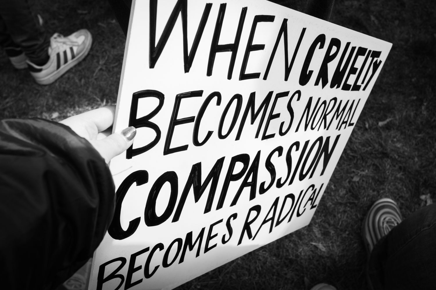 Powerful B&W documentary photography of a public protest. Handwritten sign with a personal message in a city crowd. Authentic news imagery.