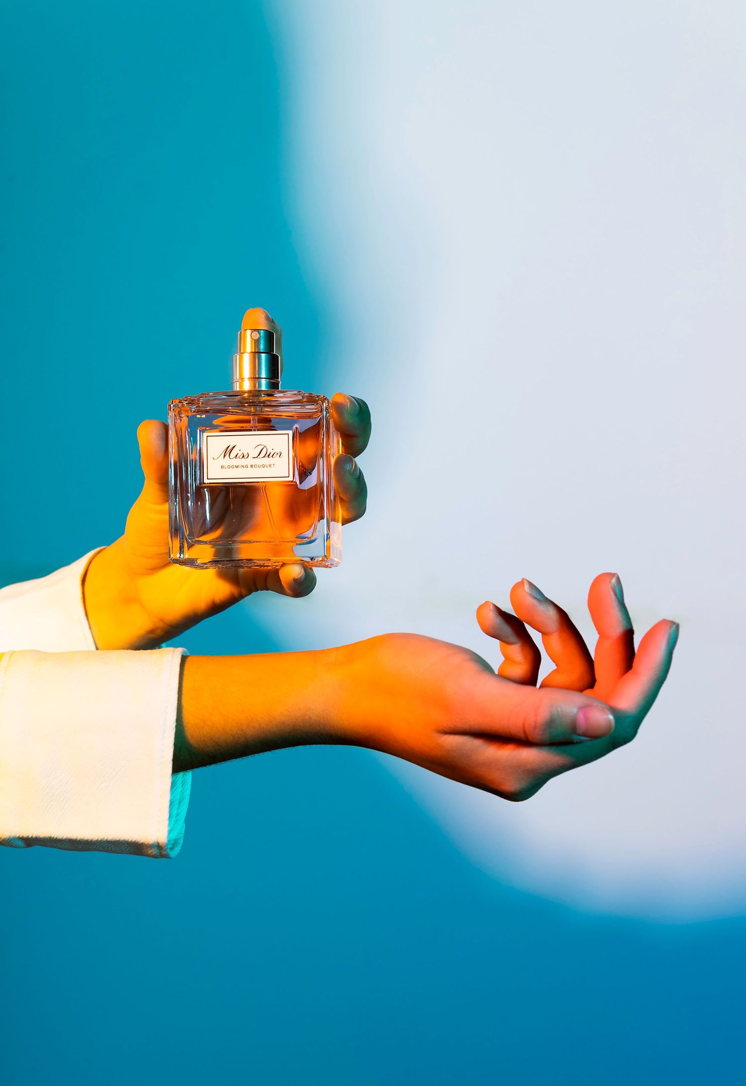 Vibrant product photography of a Miss Dior perfume bottle, utilizing warm, directional light and creative hand-modeling for luxury brand