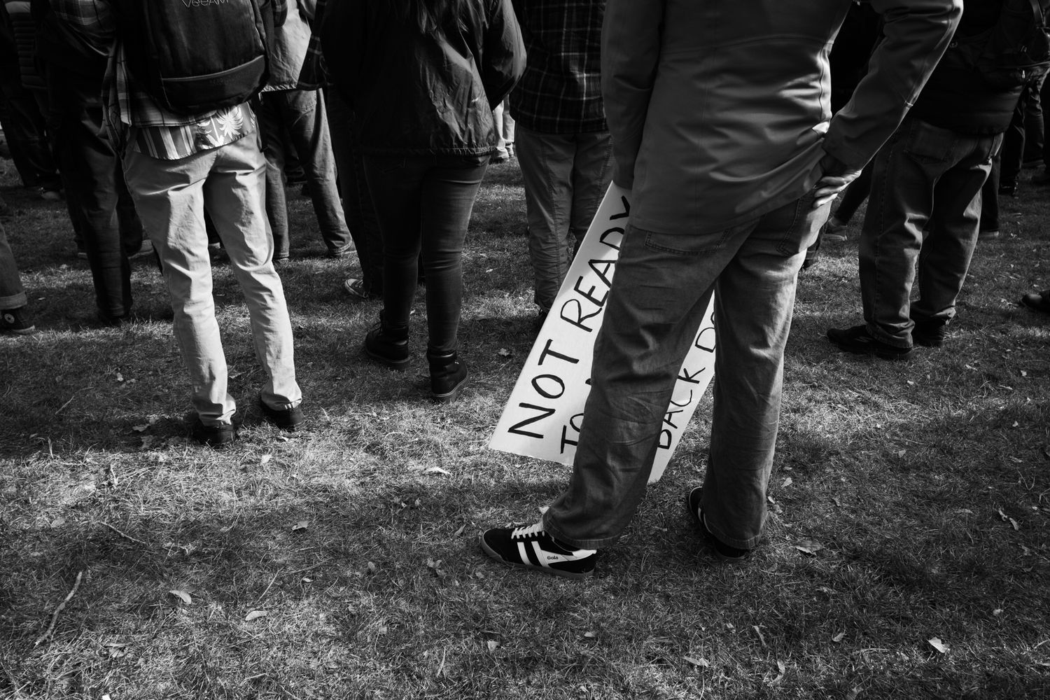 Candid B&W documentary photography of a protester holding a sign at a public march. Authentic street-level imagery for news and editorial.