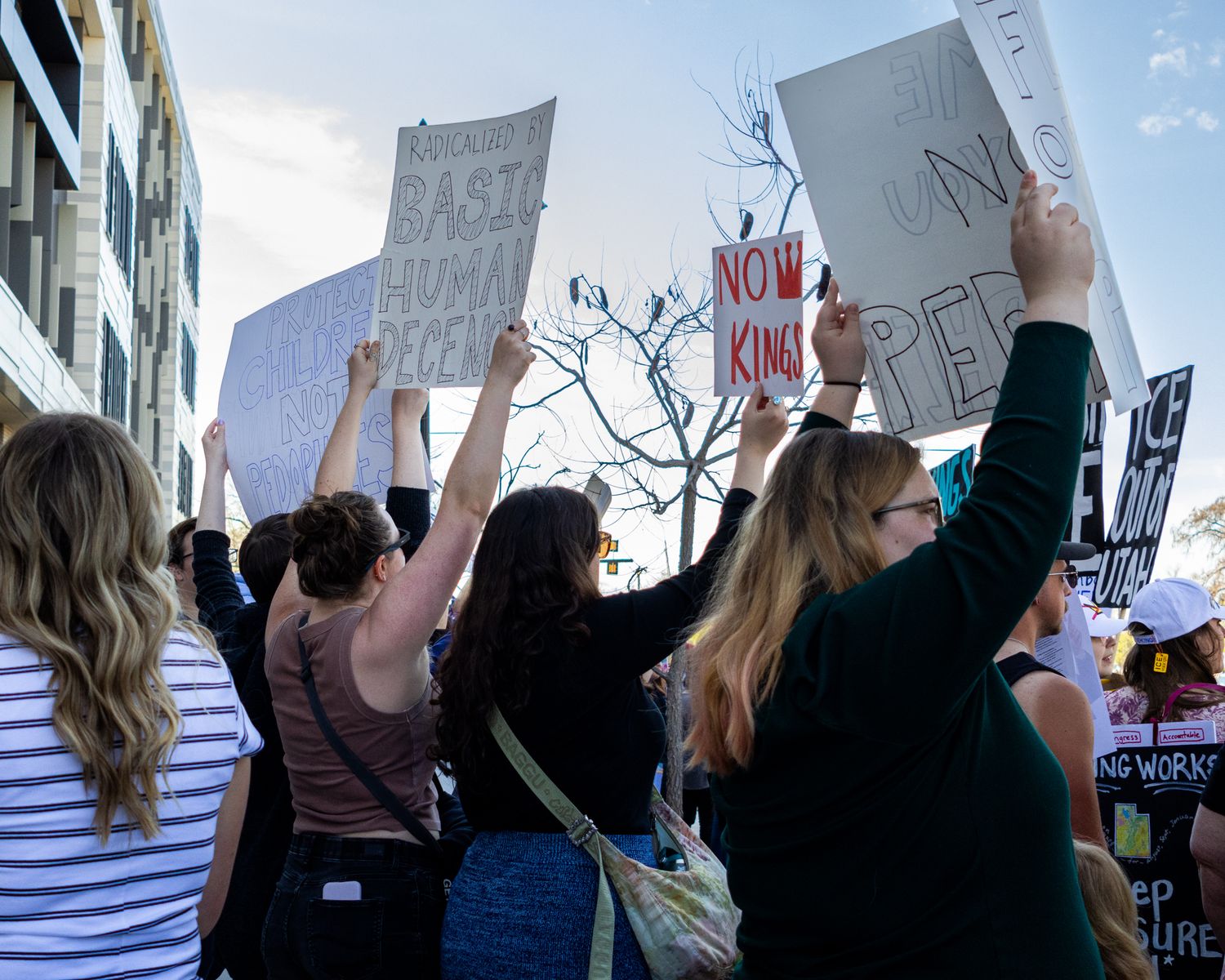 A candid shot of public advocacy, capturing the collective energy of a crowd and the power of hand-lettered signs against an urban backdrop.