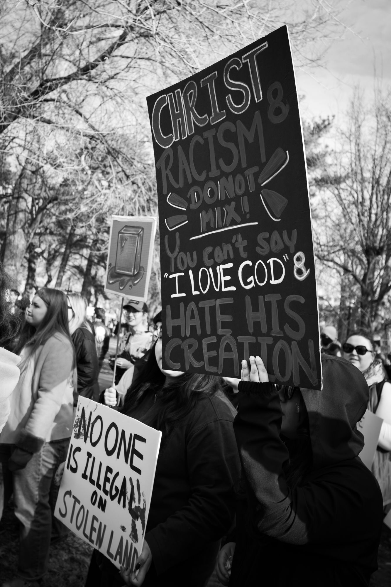 Powerful B&W documentary photography of a public protest. Handwritten sign with a personal message in a city crowd. Authentic news imagery.