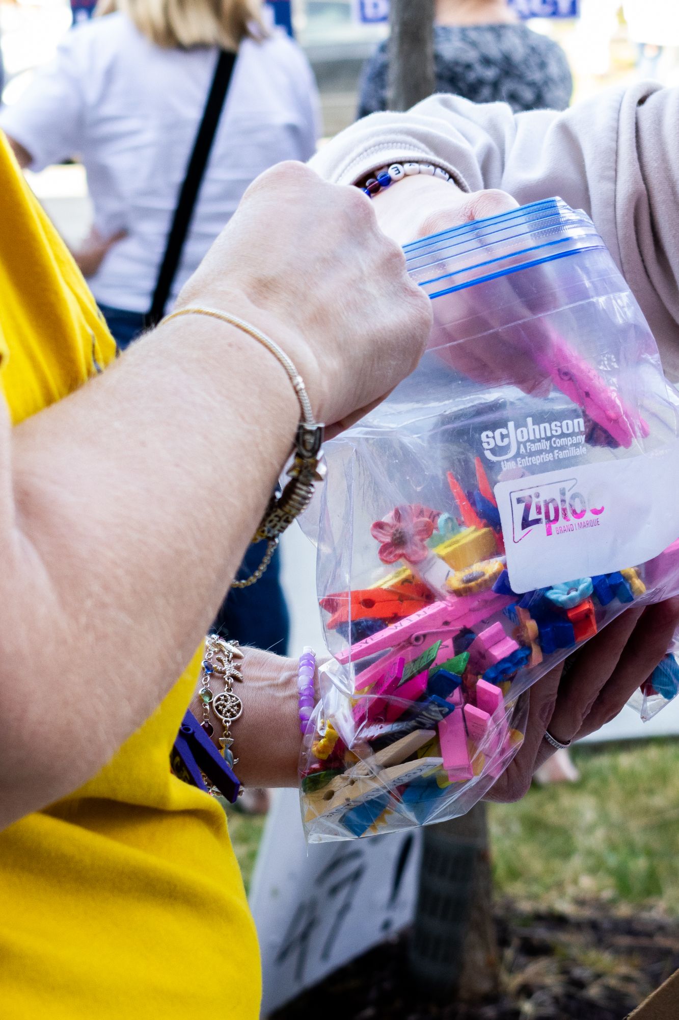 A close-up documentary shot capturing a moment of community exchange, featuring hands reaching into a bag of colorful, handmade trinkets.
