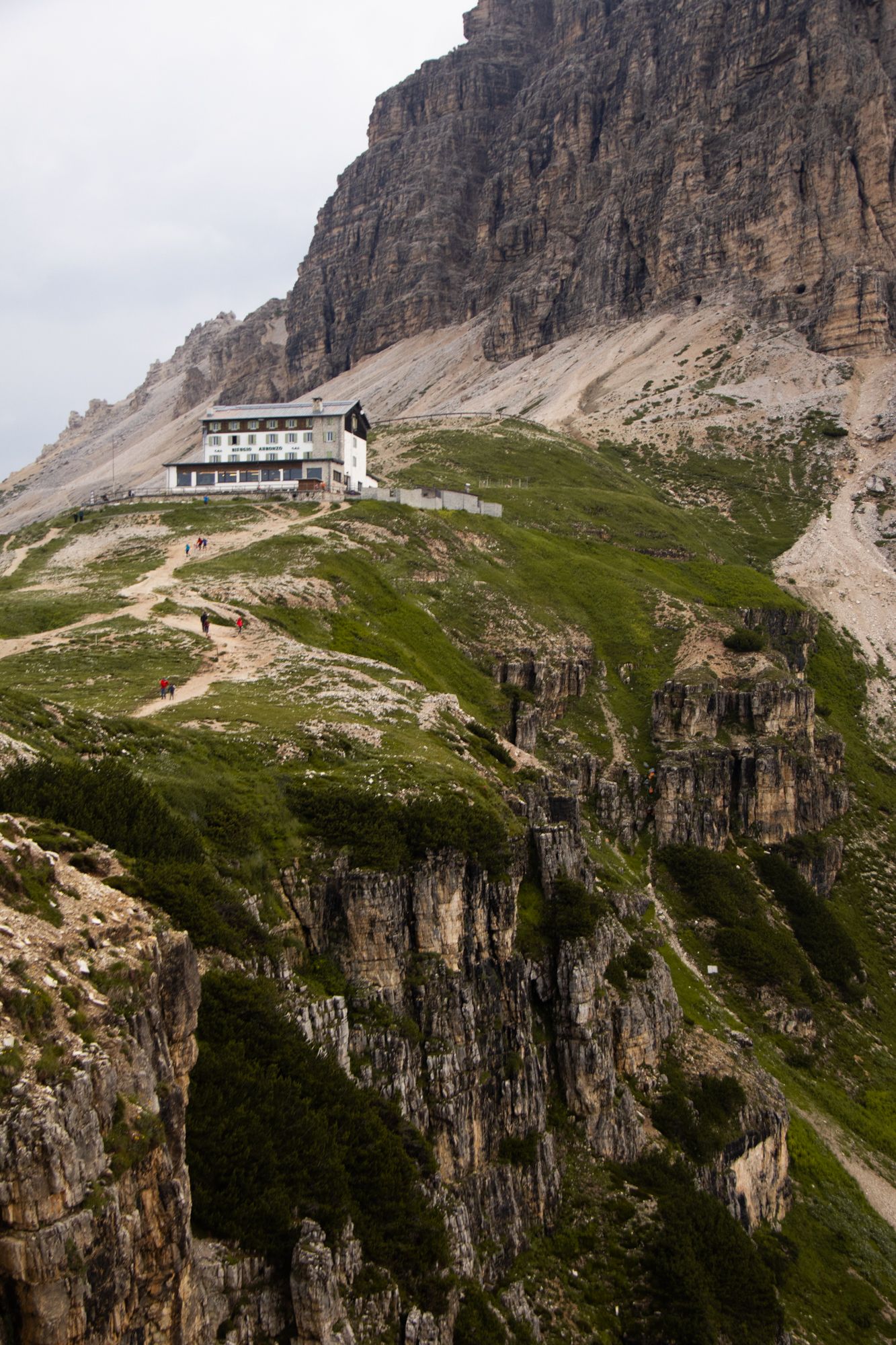 Dramatic alpine scene of a mountain refuge perched on rugged cliffs beneath towering Dolomite peaks. Iconic high-altitude landscape.