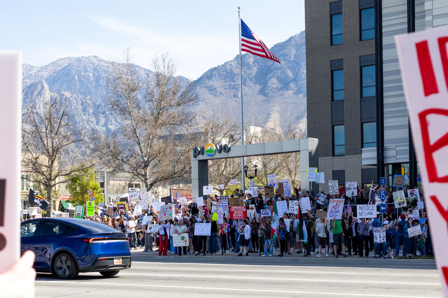 A wide-angle documentary shot capturing a large-scale public protest in Provo, Utah, with the iconic mountain peaks.