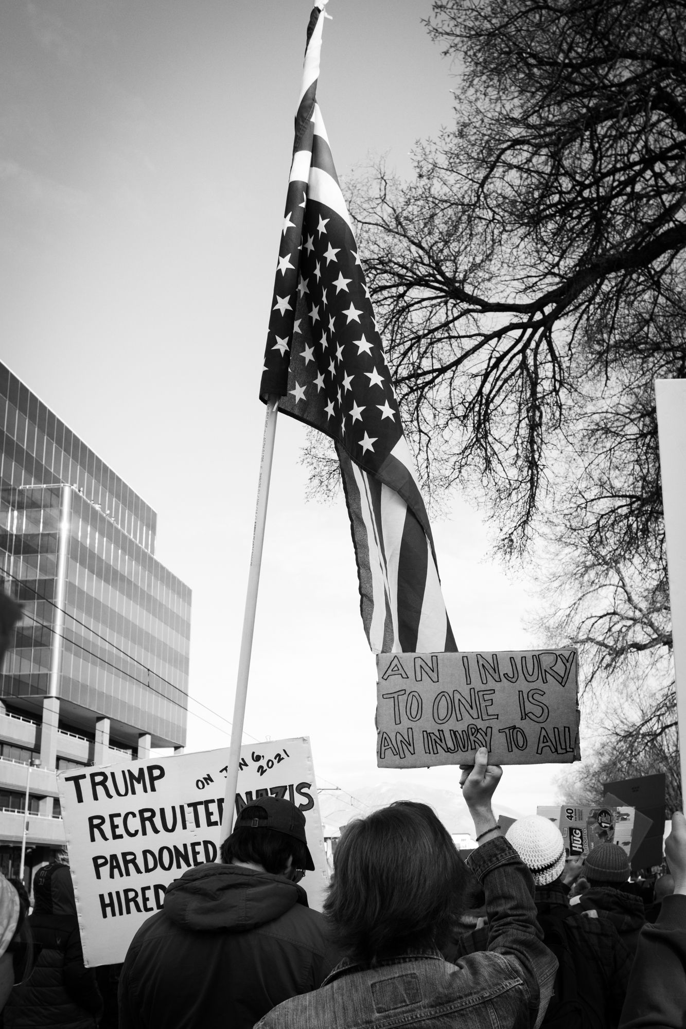 Powerful B&W documentary photography of a city protest. American flag and handwritten signs in an urban setting. Authentic news imagery.