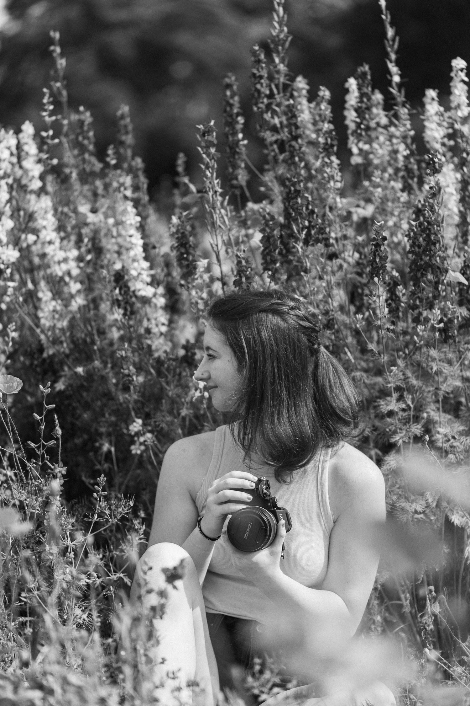 Black and white portrait of photographer with camera among tall wildflowers.