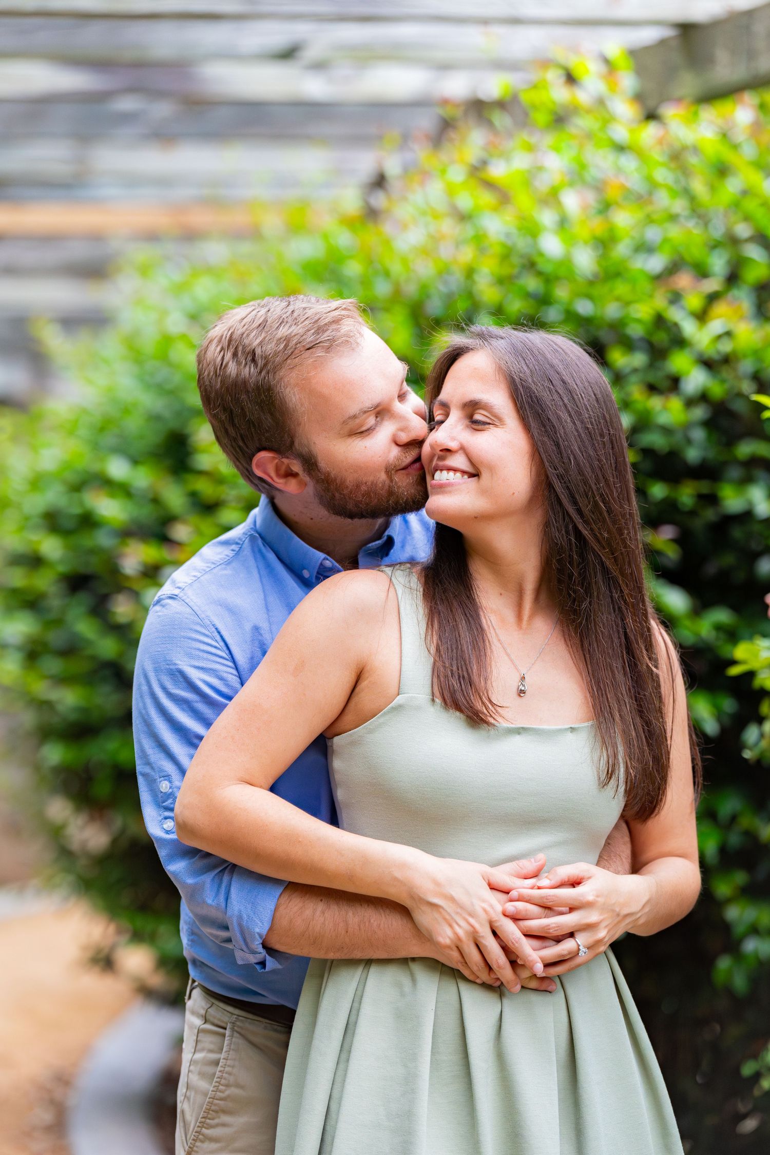 A couple embraces in a garden setting with lush greenery in the background.