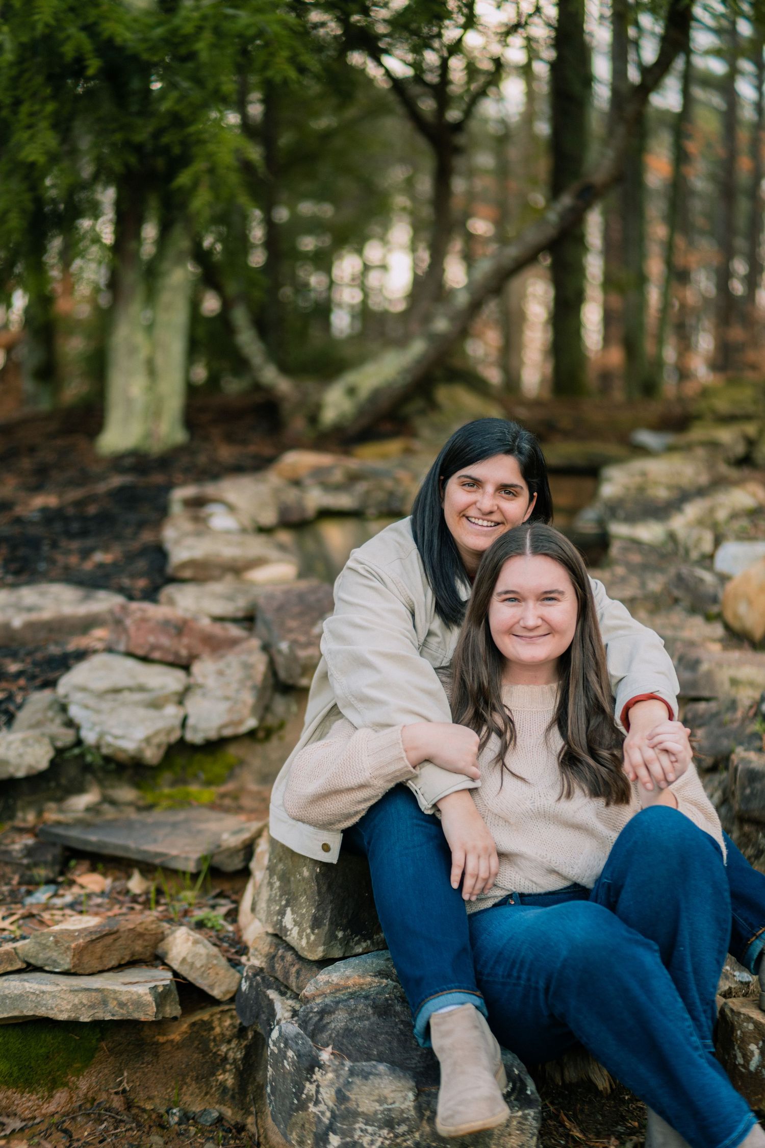 Two people share a cozy moment while sitting on rocky terrain surrounded by nature.