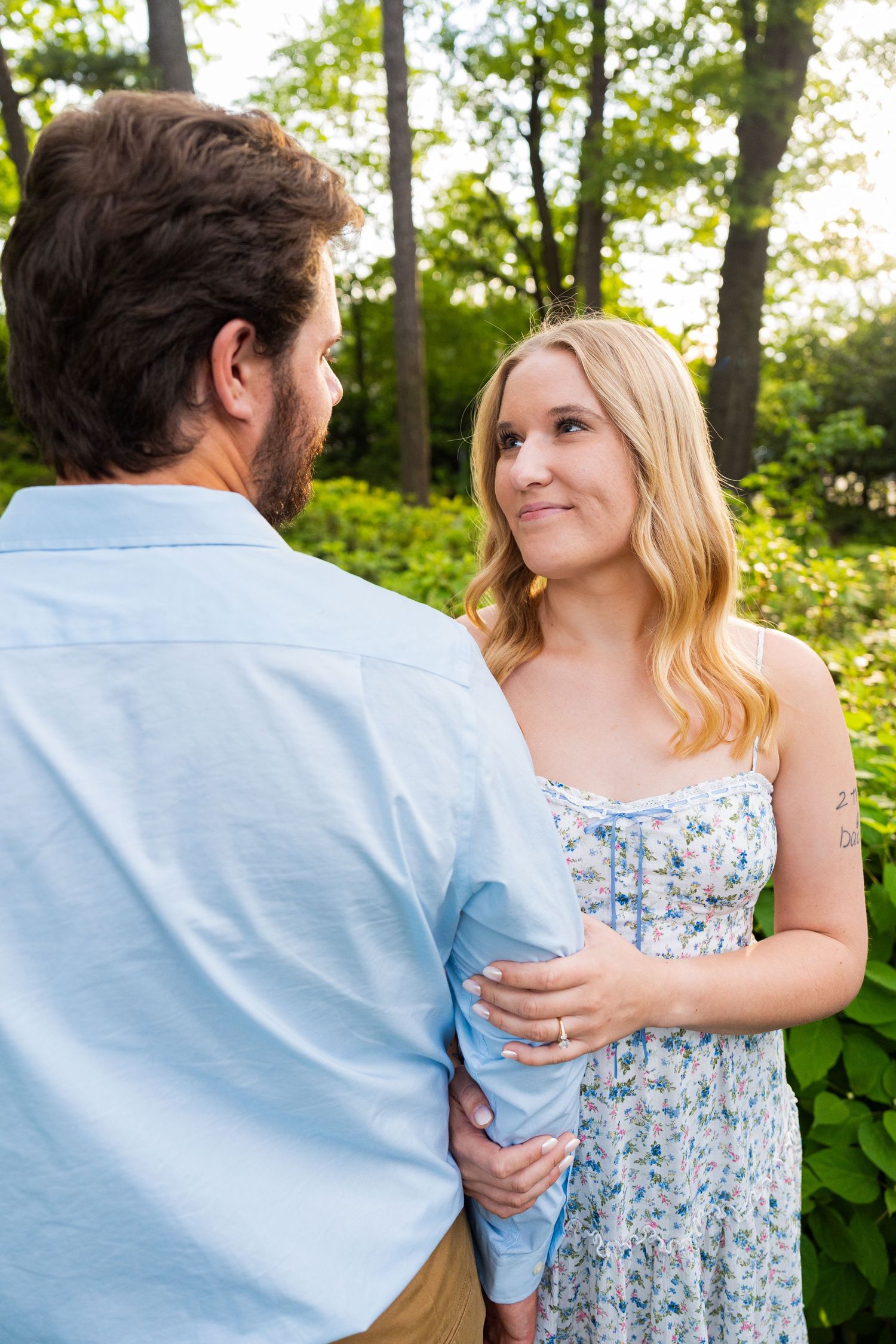A romantic outdoor scene of a couple gazing at each other on a sunny day surrounded by lush greenery.