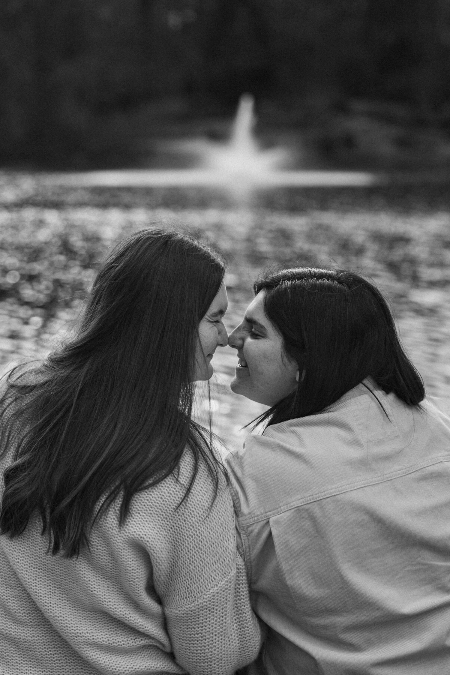 A black and white photo captures an intimate moment by a tranquil lake with sunlight reflection.