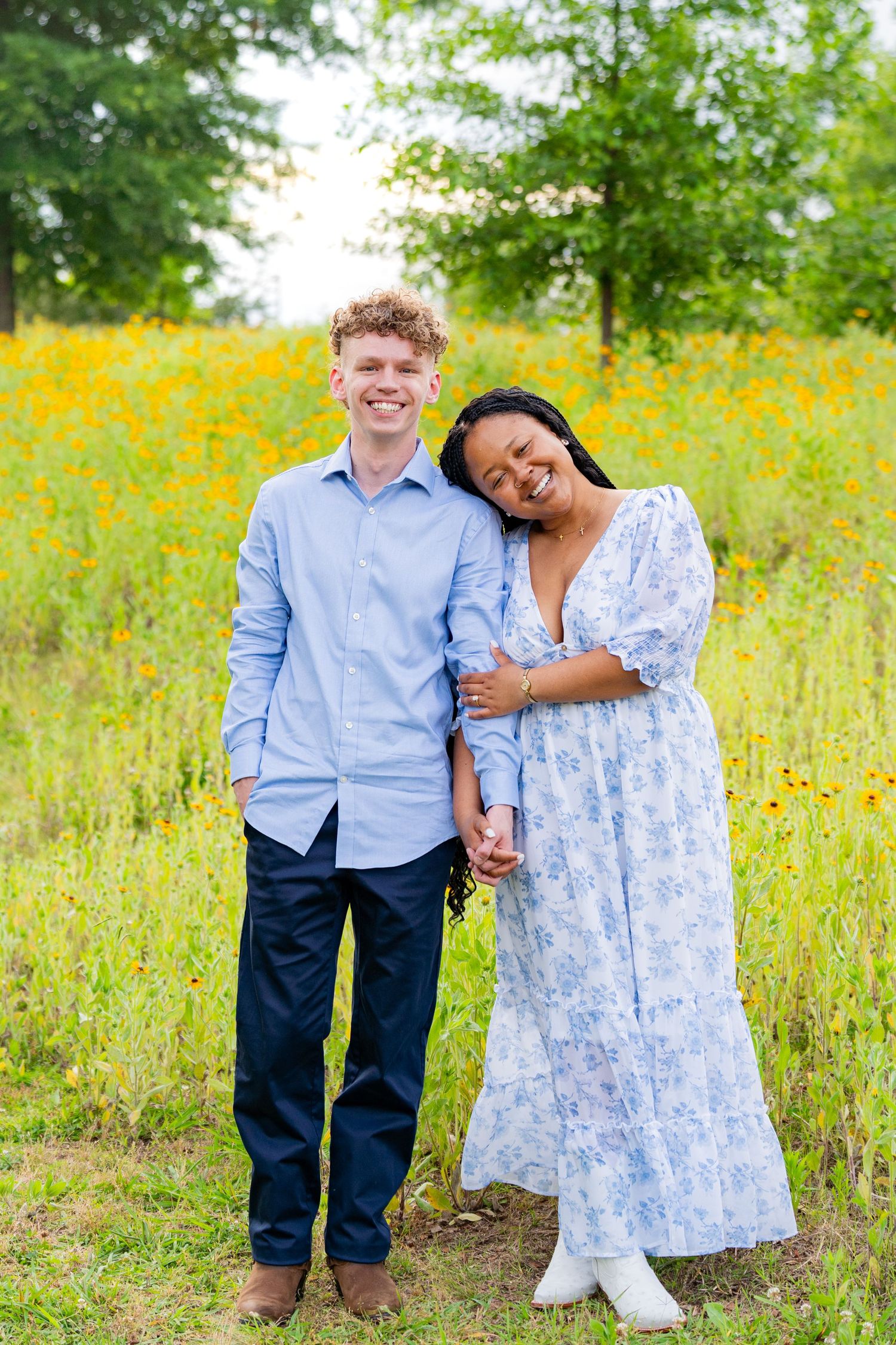 Couple standing together in a field of yellow wildflowers on a sunny day.