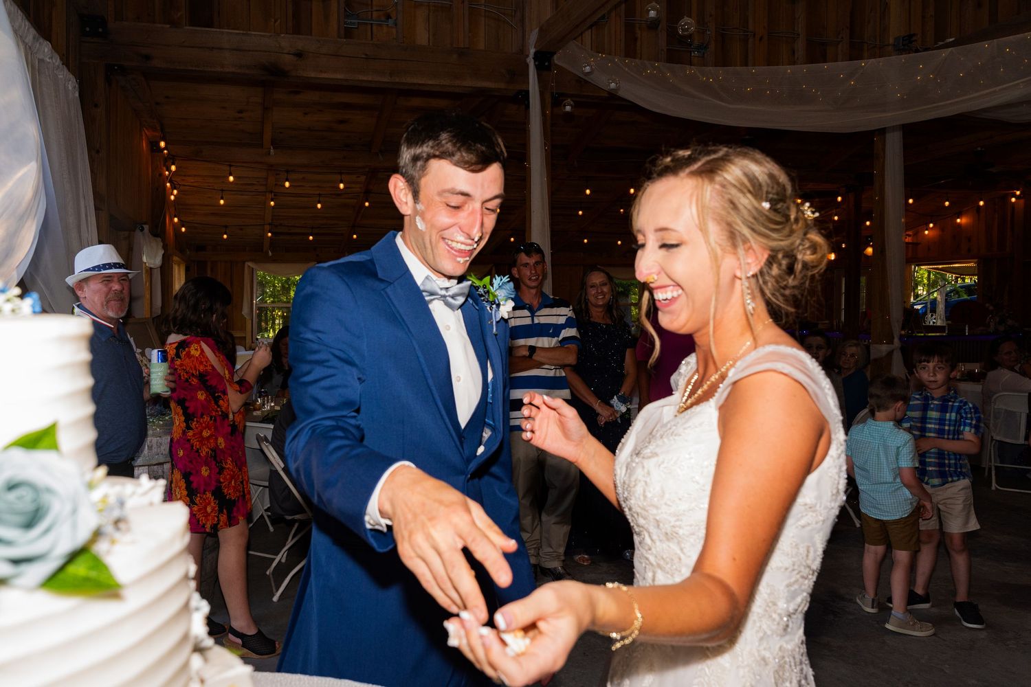 Joyful pair laughing and dancing together in an event venue with string lights and rustic decor.
