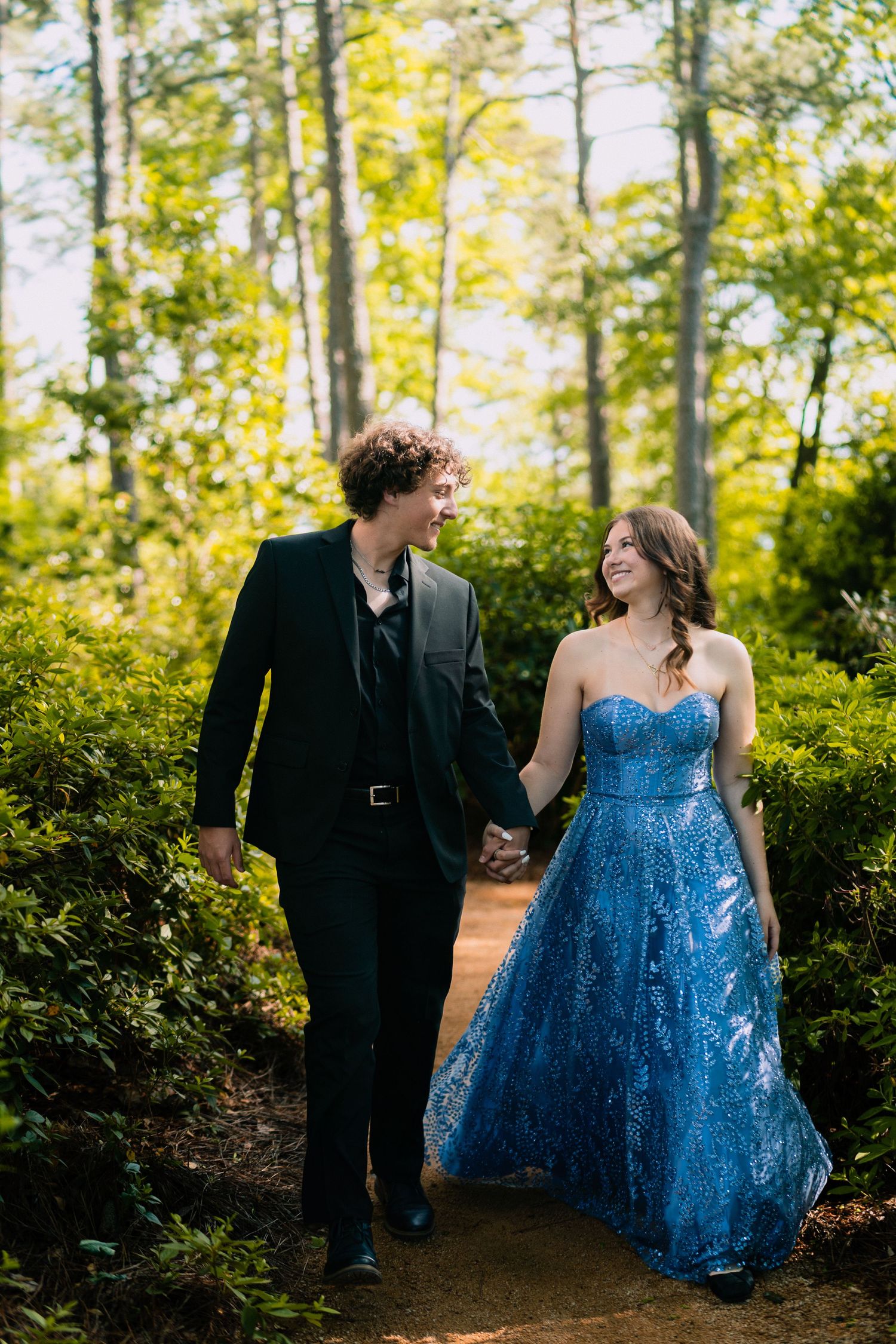Couple walking hand in hand on a forest path, with her wearing a sparkly blue gown.