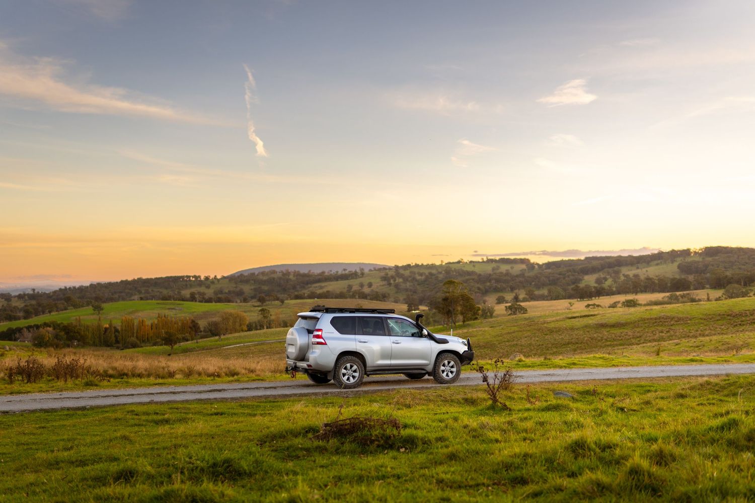 White Toyota Land Cruiser Prado on scenic countryside road at sunset.