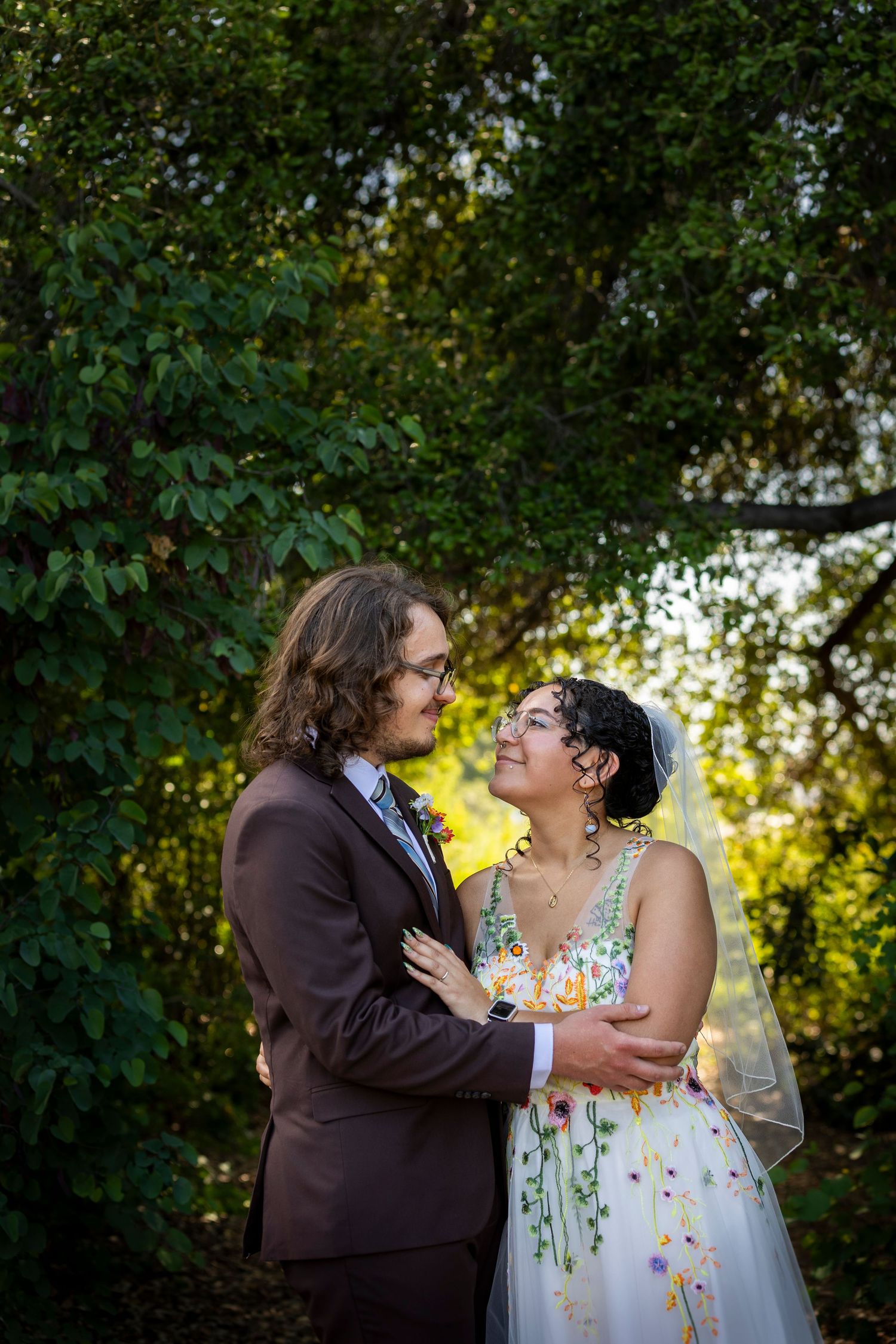 A romantic couple sharing tender moments in a garden setting during their wedding wearing a dark suit and floral dress.