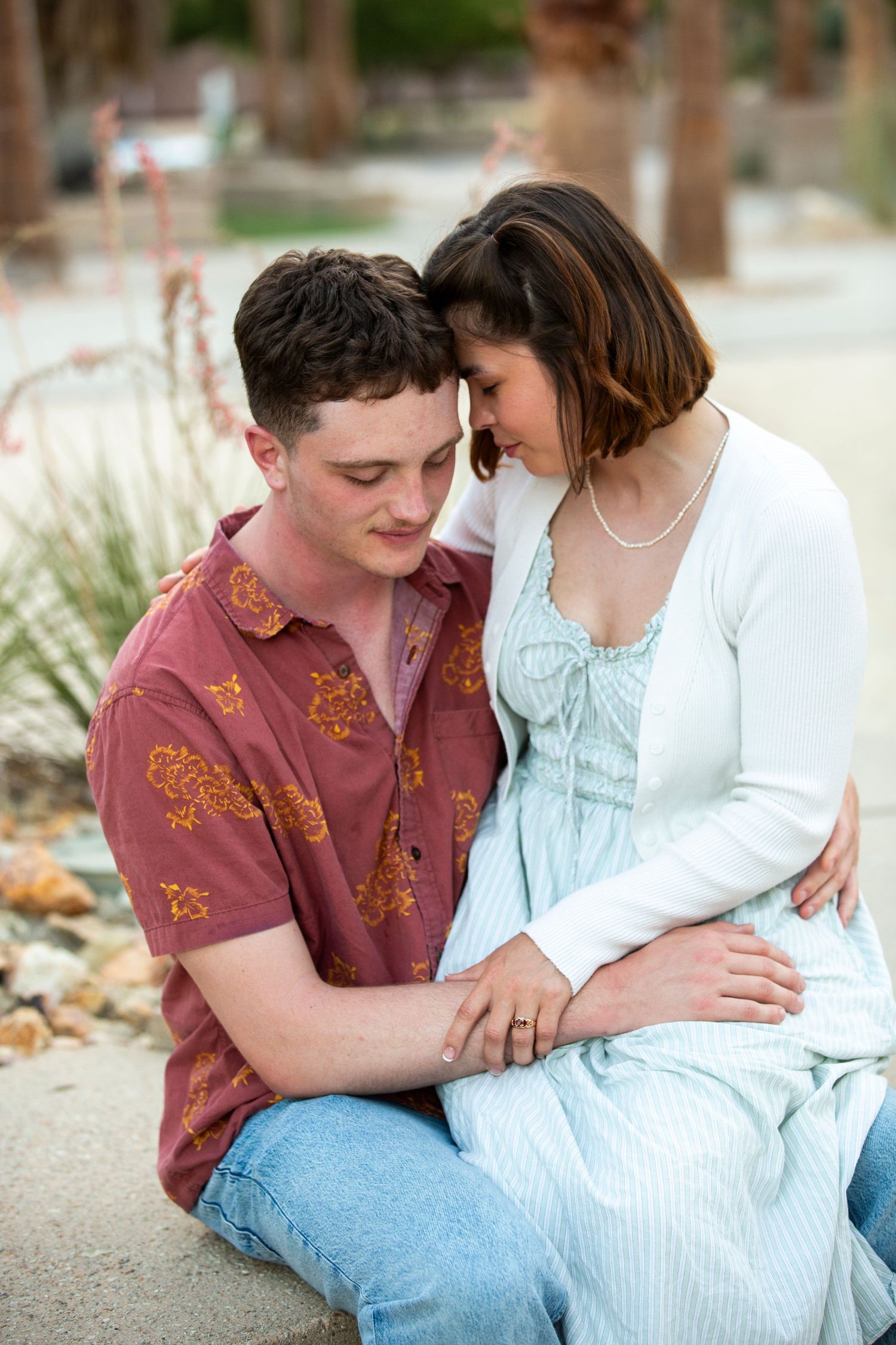 A romantic couple shares an intimate moment while sitting outdoors in casual attire.