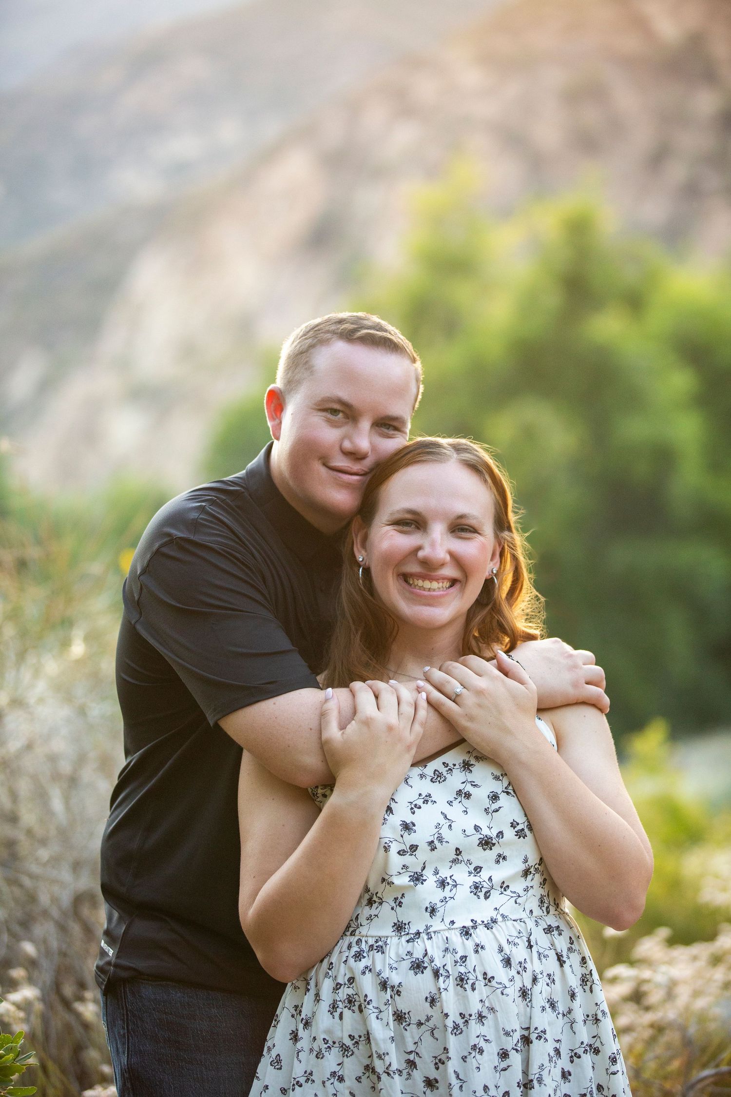 Couple embraces outdoors in natural setting during romantic maternity photo session in sunlit meadow.