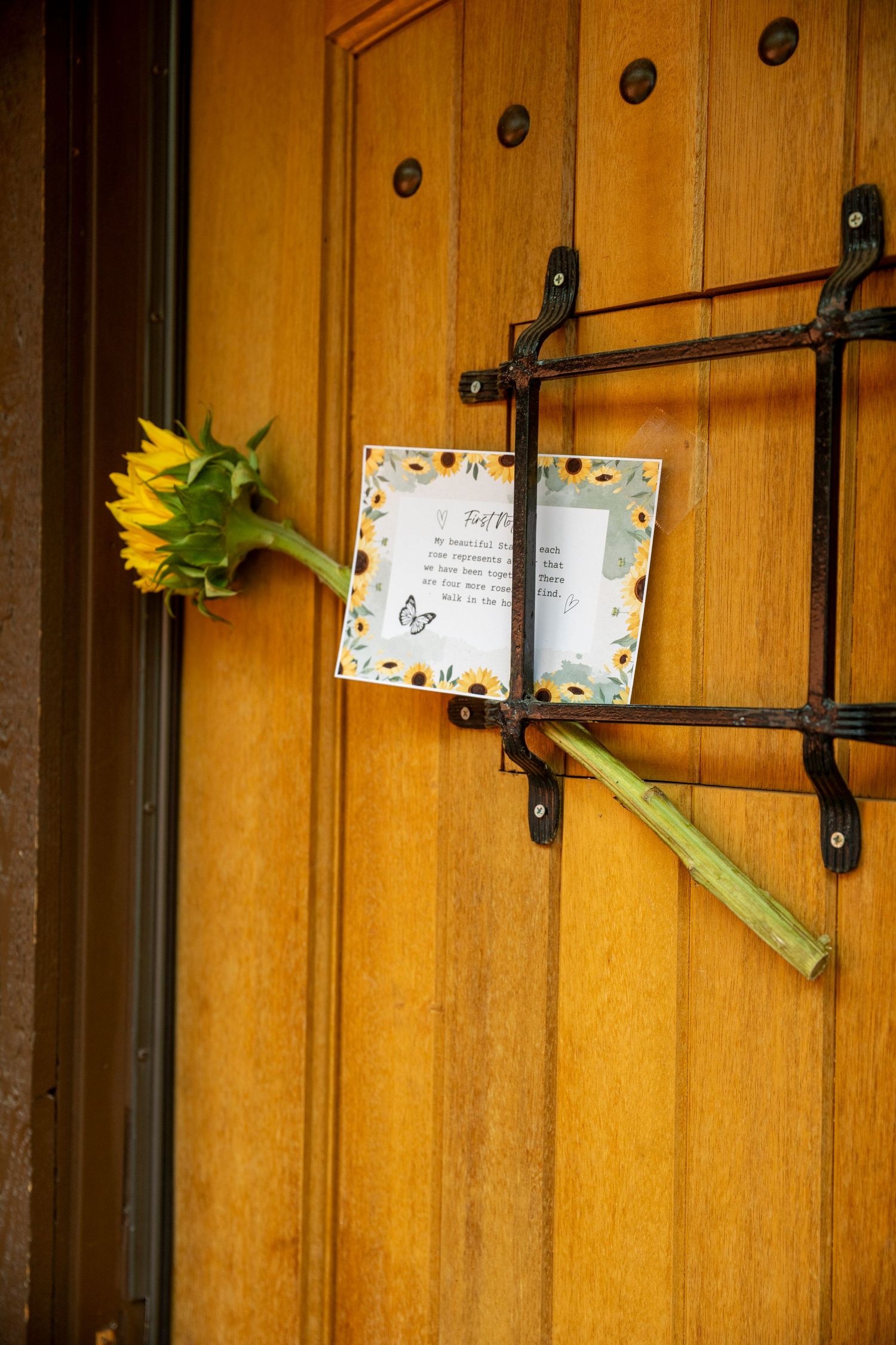 Sunflowers peek through a rustic wooden door with decorative iron hardware and butterfly wall art.