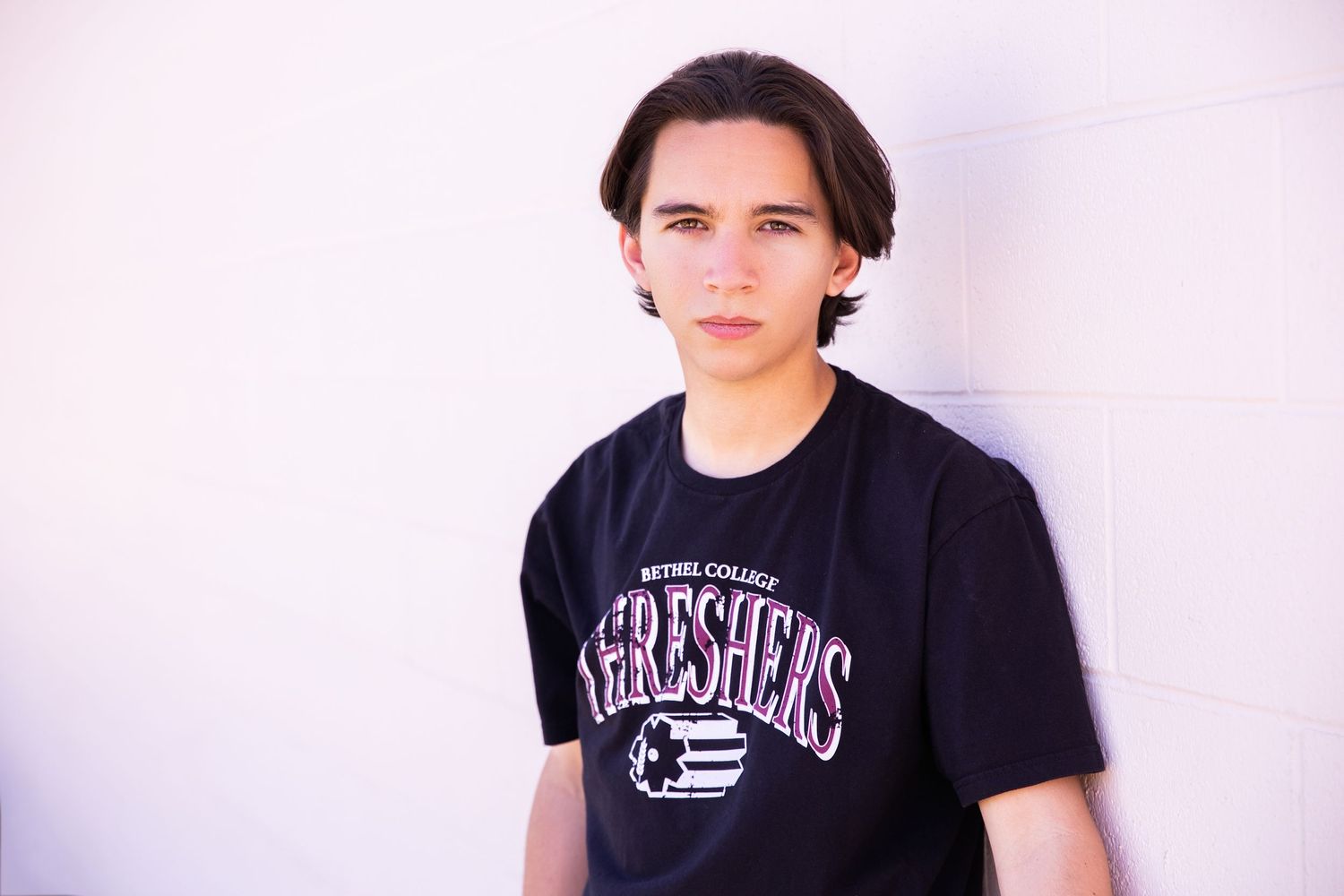 Senior Portrait in his new College t-shirt poses against a light background at University of Redlands sports area. Palm Springs Photographer
