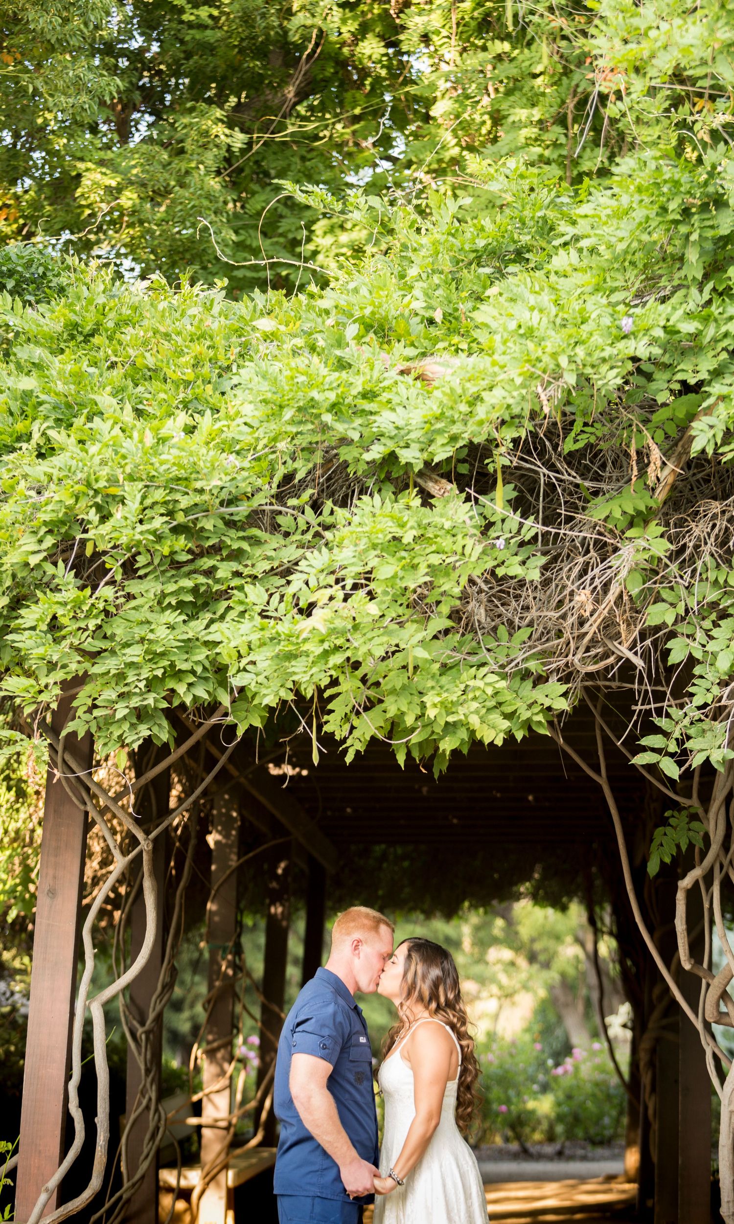 Romantic couple embracing under a lush green garden archway during a summer day.