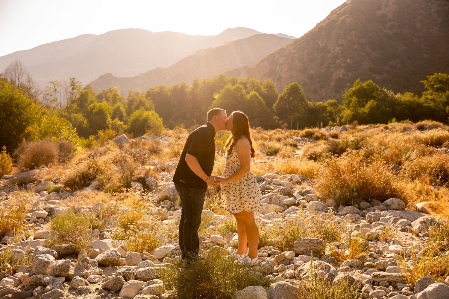 Beautiful sunset silhouettes couple standing in golden desert landscape with mountains in background.