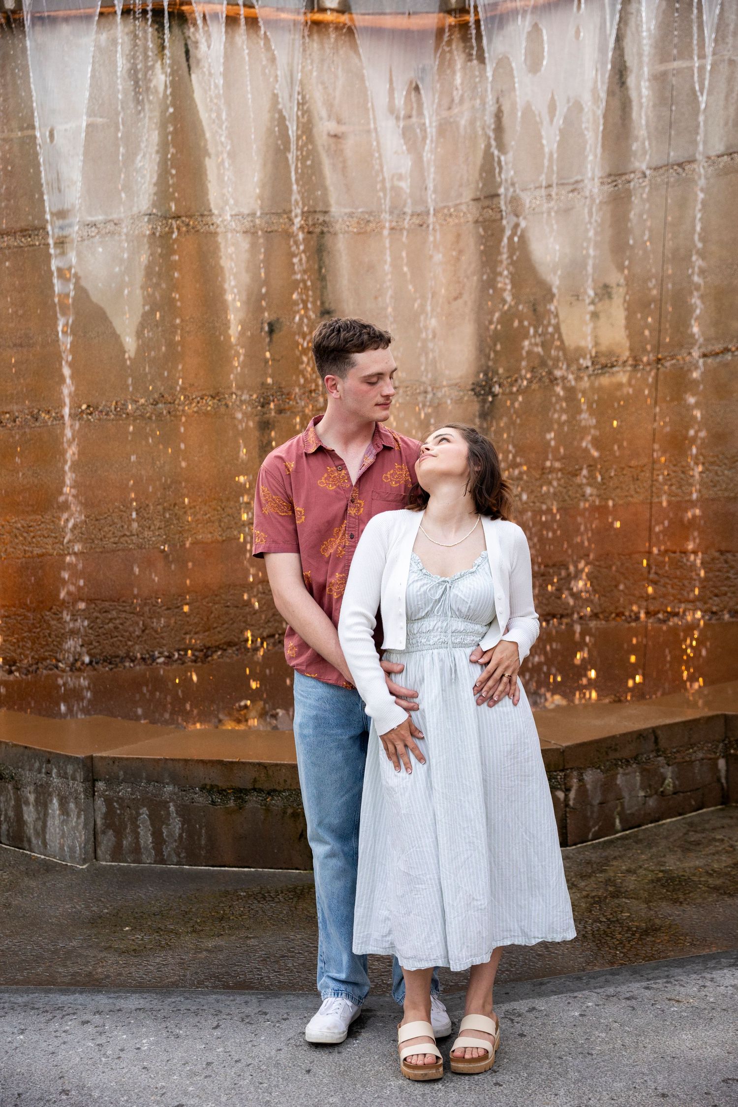 A couple share a joyful moment together against a rustic metal wall background in casual summer attire.