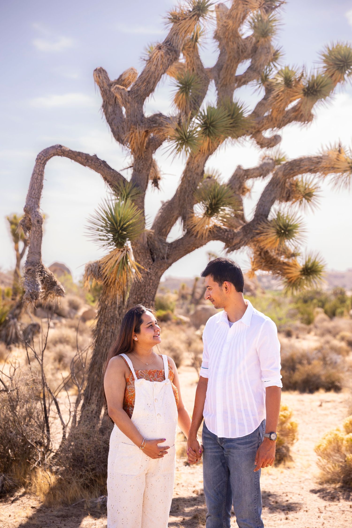 Couples pose playfully in a desert landscape with Joshua trees creating a romantic desert photoshoot setting.
