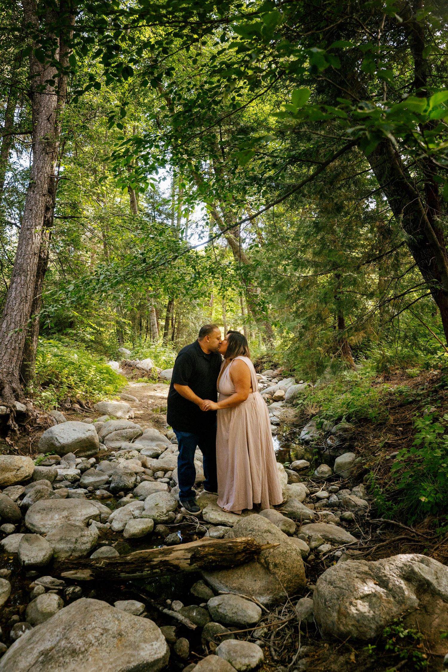 A couple shares intimate moments on rocky terrain surrounded by lush greenery in a romantic forest setting.